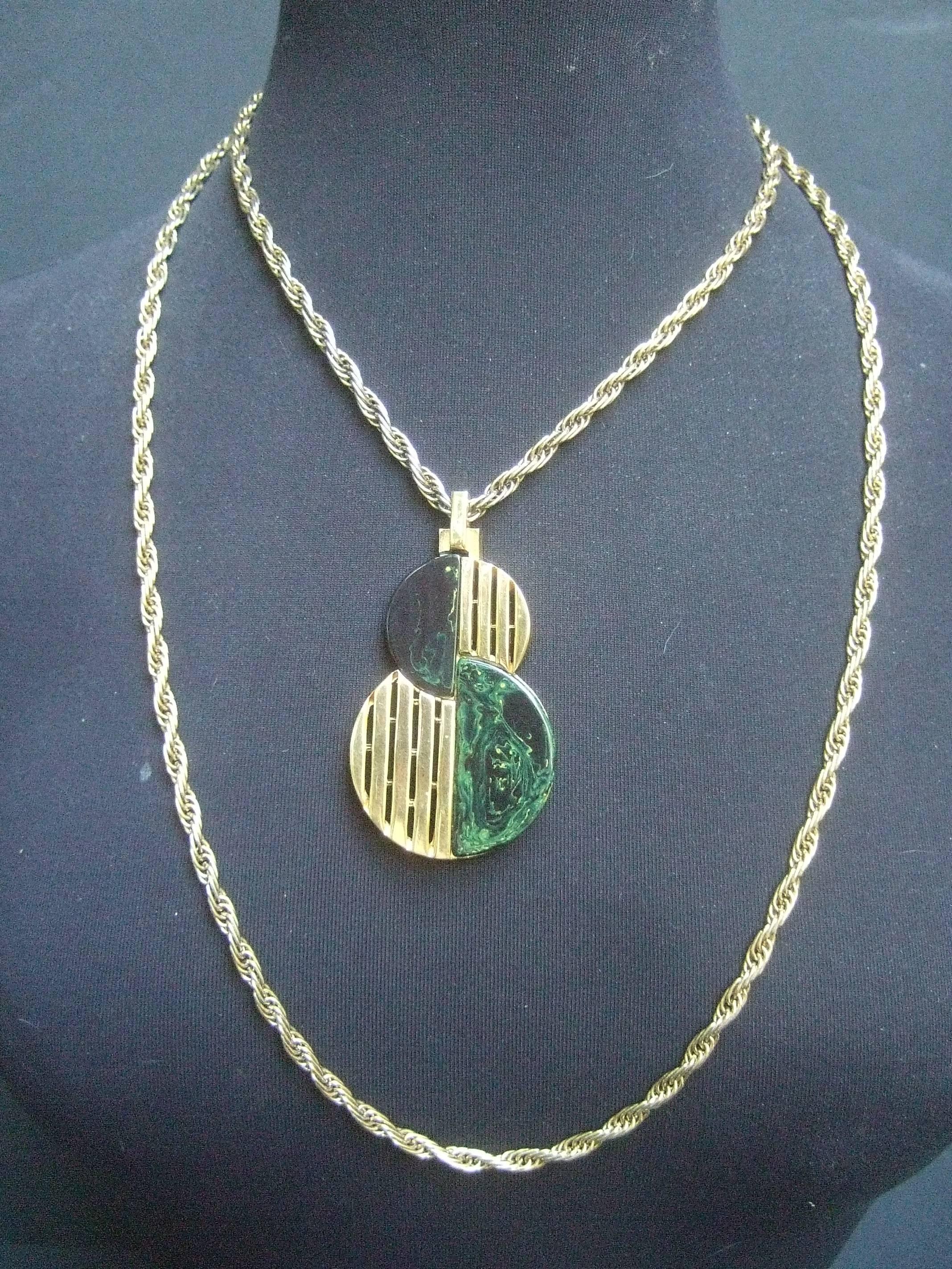 Trifari Sleek gilt metal lucite pendant necklace c 1970
The minimalist necklace is designed with    
a circular pendant

The severe pendant is designed with vertical
gilt metal bands juxtaposed with green lucite
marbleized tiles that emulate