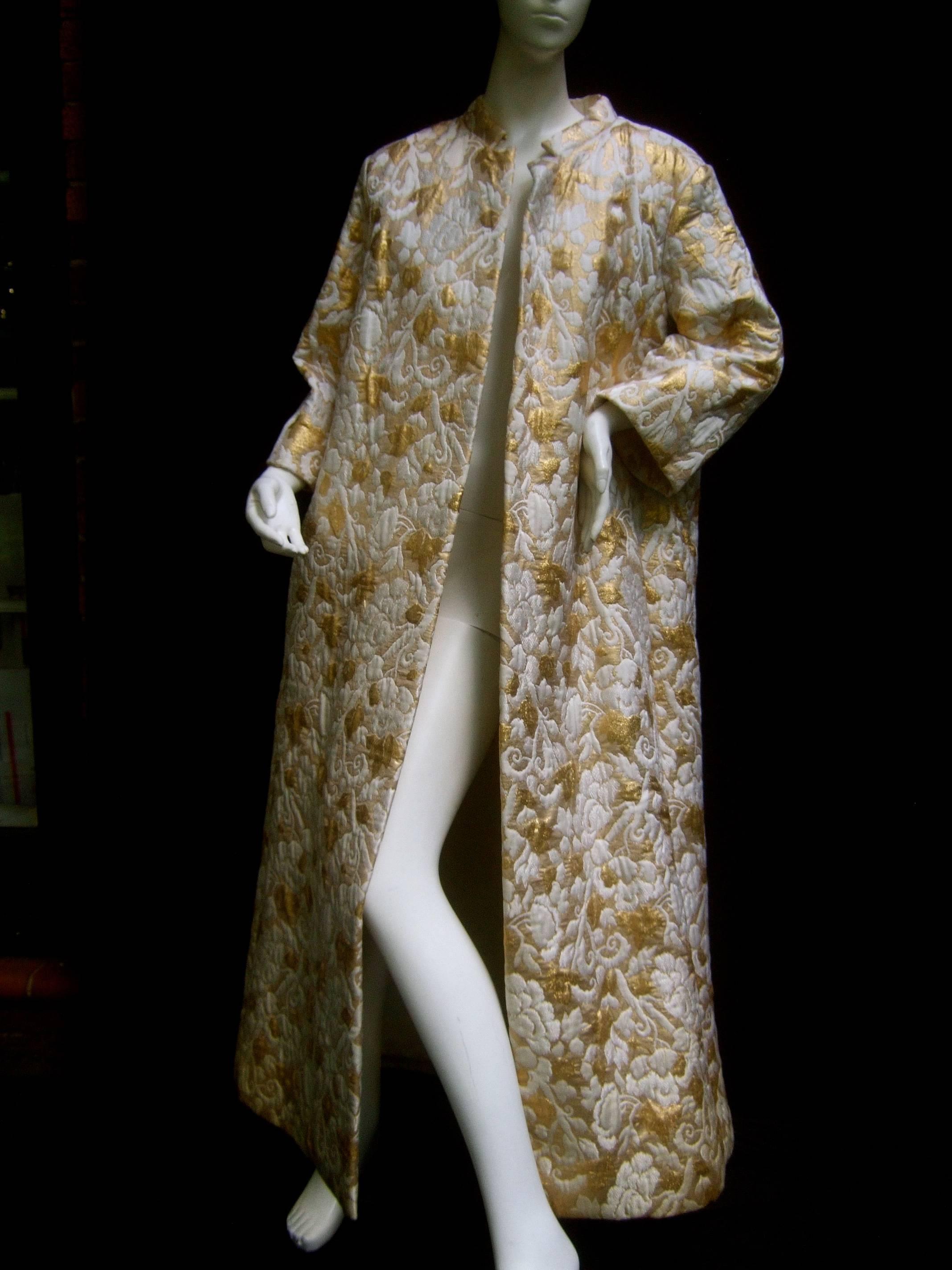 Opulent gold & white brocade opera coat c 1960 
The elegant maxi style evening coat is designed 
with luxurious heavy brocade fabric 

The garden of sinuous flowers are a combination 
of subdued white blooms juxtaposed with vibrant 
gold