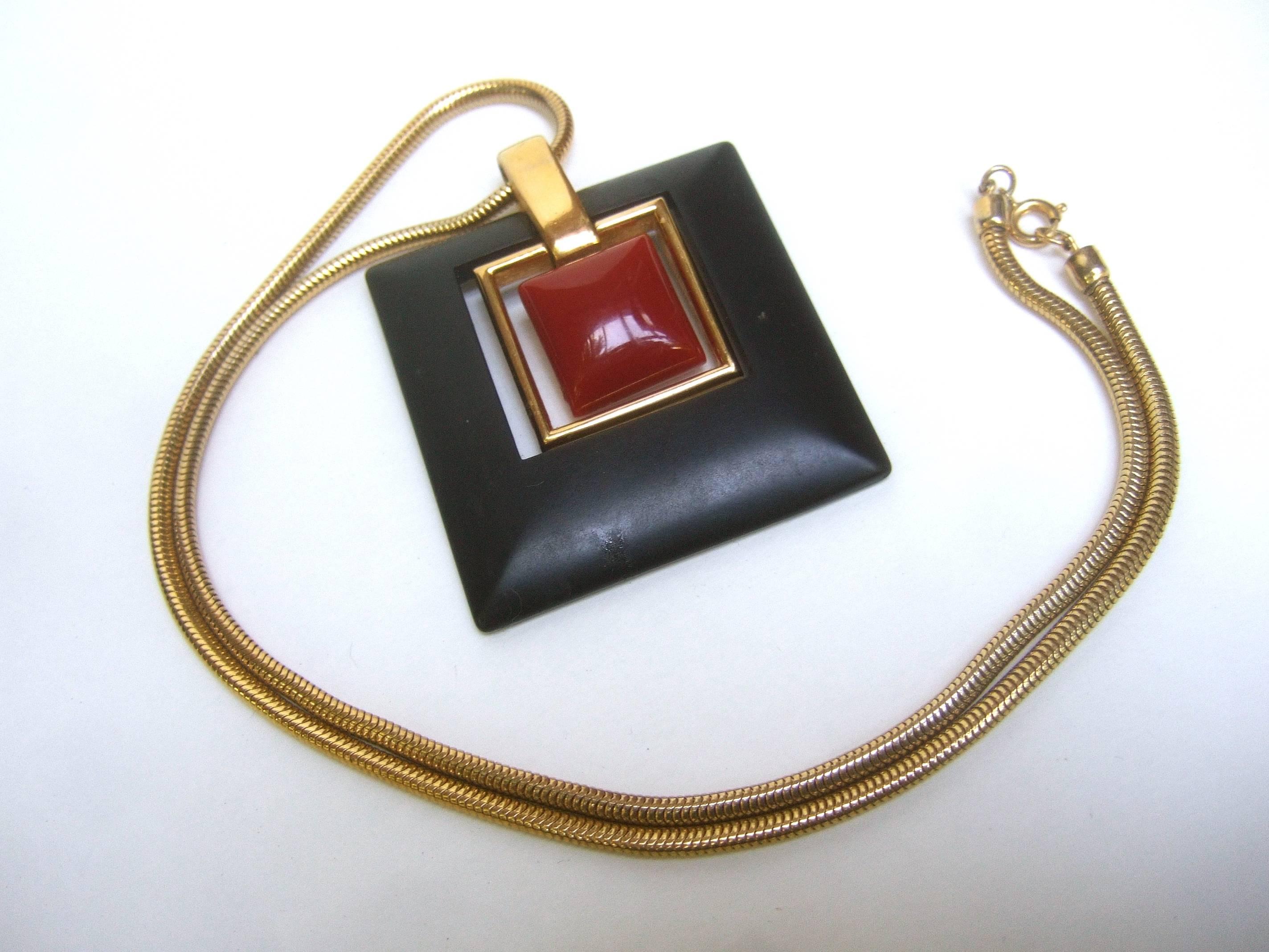 Trifari Mod cinnabar & ebony resin pendant necklace c 1970 
The severe bold design has a center cinnabar color
lucite tile framed with gilt metal and a large black
resin border

The large geometric pendant is suspended from a slinky 
gilt