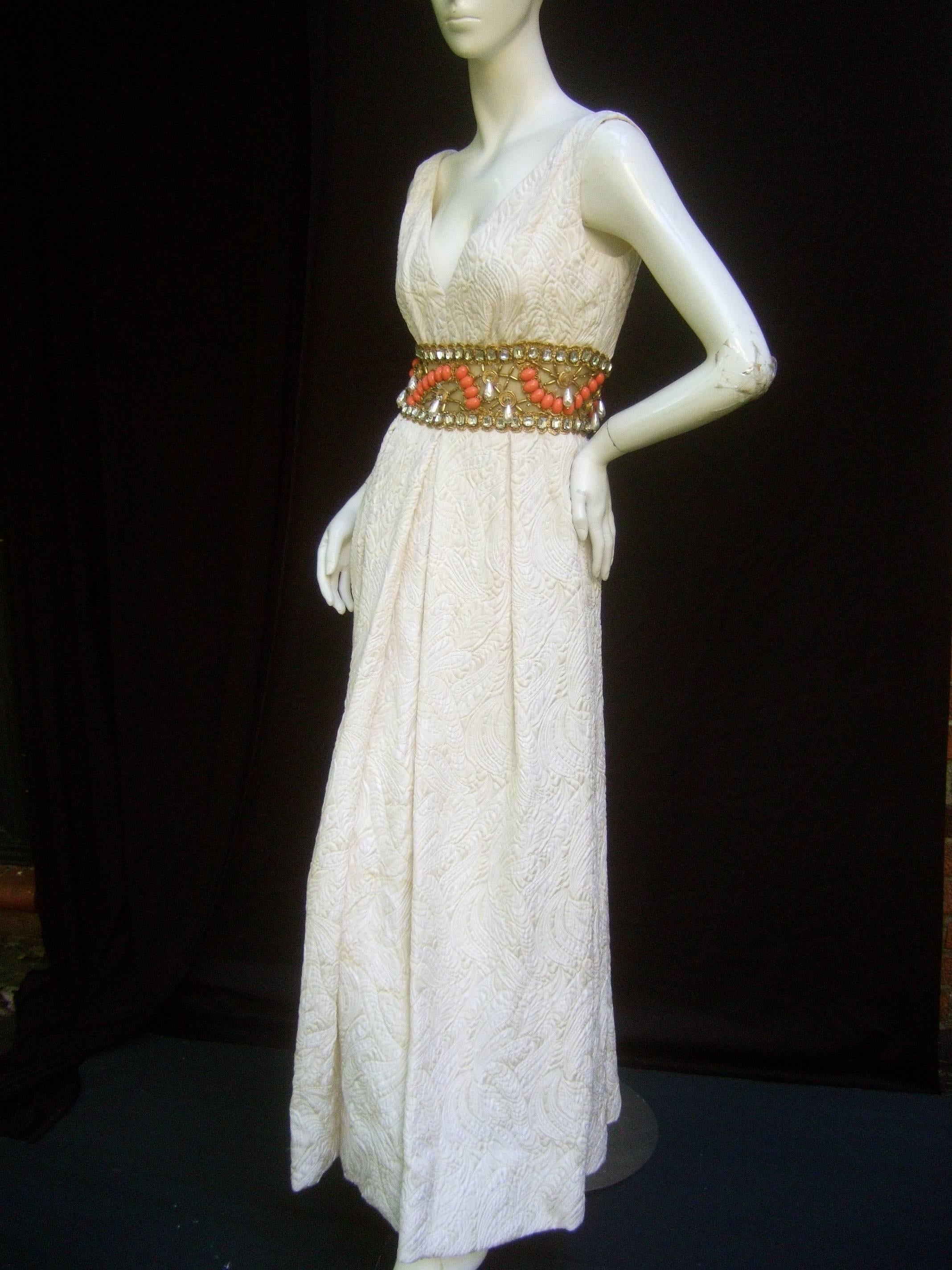 Jewell Chapman Étonnante robe empire ornée de bijoux en brocart ivoire c. années 1960
La robe de brocart exquise est conçue avec un tissu élaboré. 
Le buste est incrusté de bijoux et rehaussé de cristaux scintillants, 
pendentif en forme de