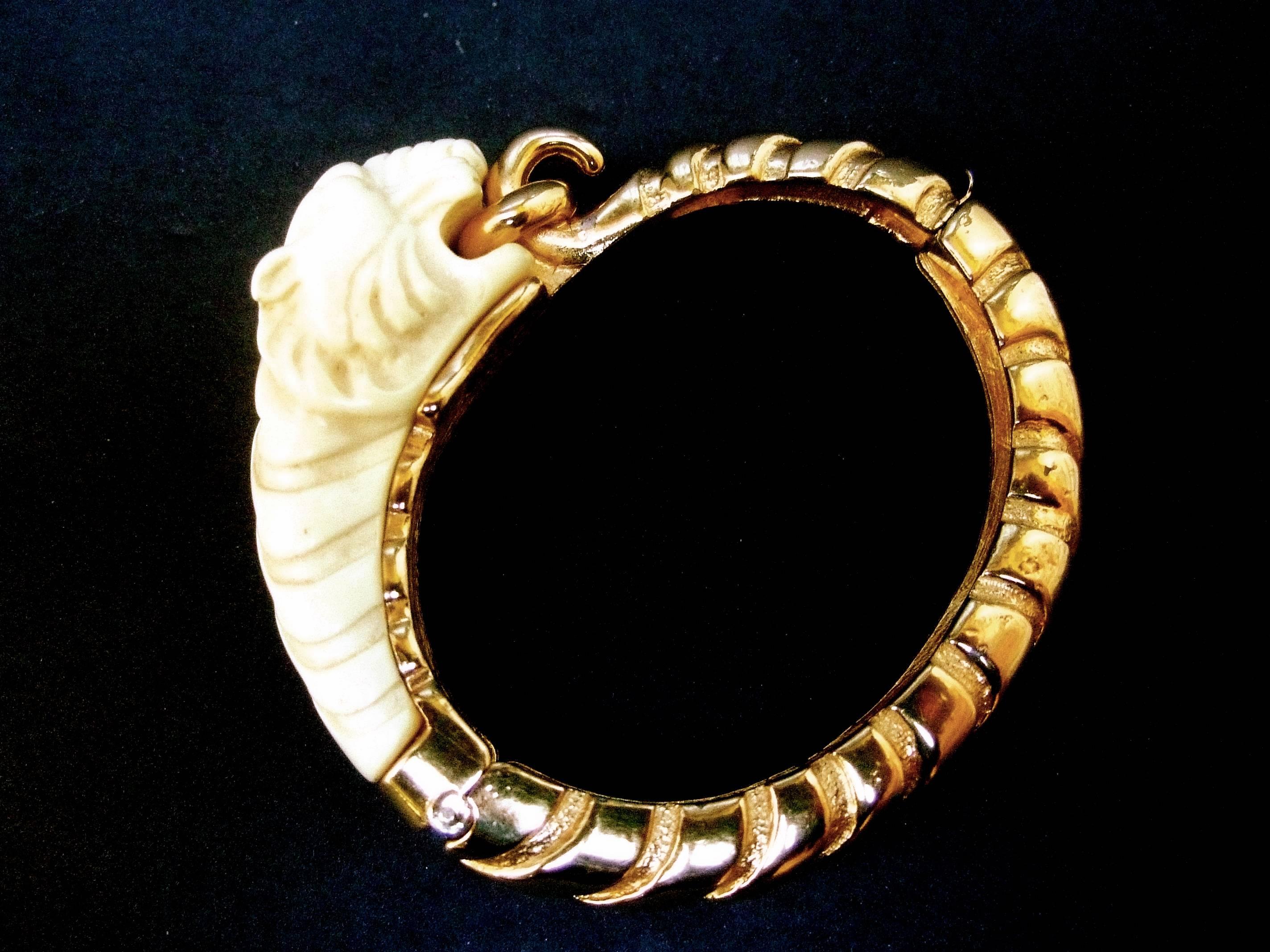 Ken Lane Sleek tiger bangle bracelet c 1970
The hinged gilt metal bracelet is designed
with an ivory color carved resin tiger's head

Cinched in the tiger's mouth is a gilt metal
ring. The sides and base of the gilt metal
hinged bangle are