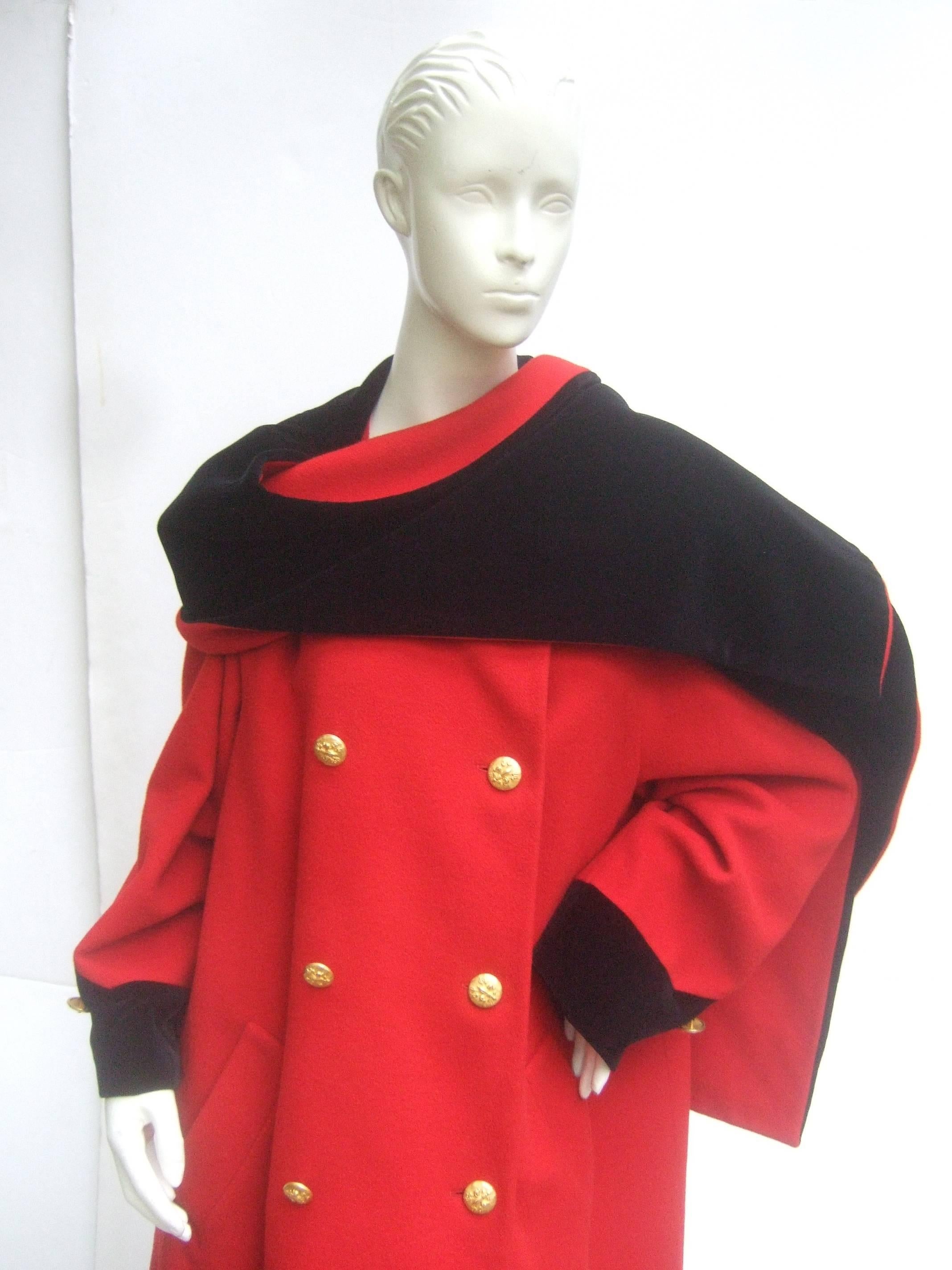 Escada Cherry red wool black velvet trim coat c 1990
The classic military style coat is designed with 
a long dramatic built in black velvet collar scarf 

The sleeve cuffs are accented with black velvet 
trim. Adorned with gilt metal insignia