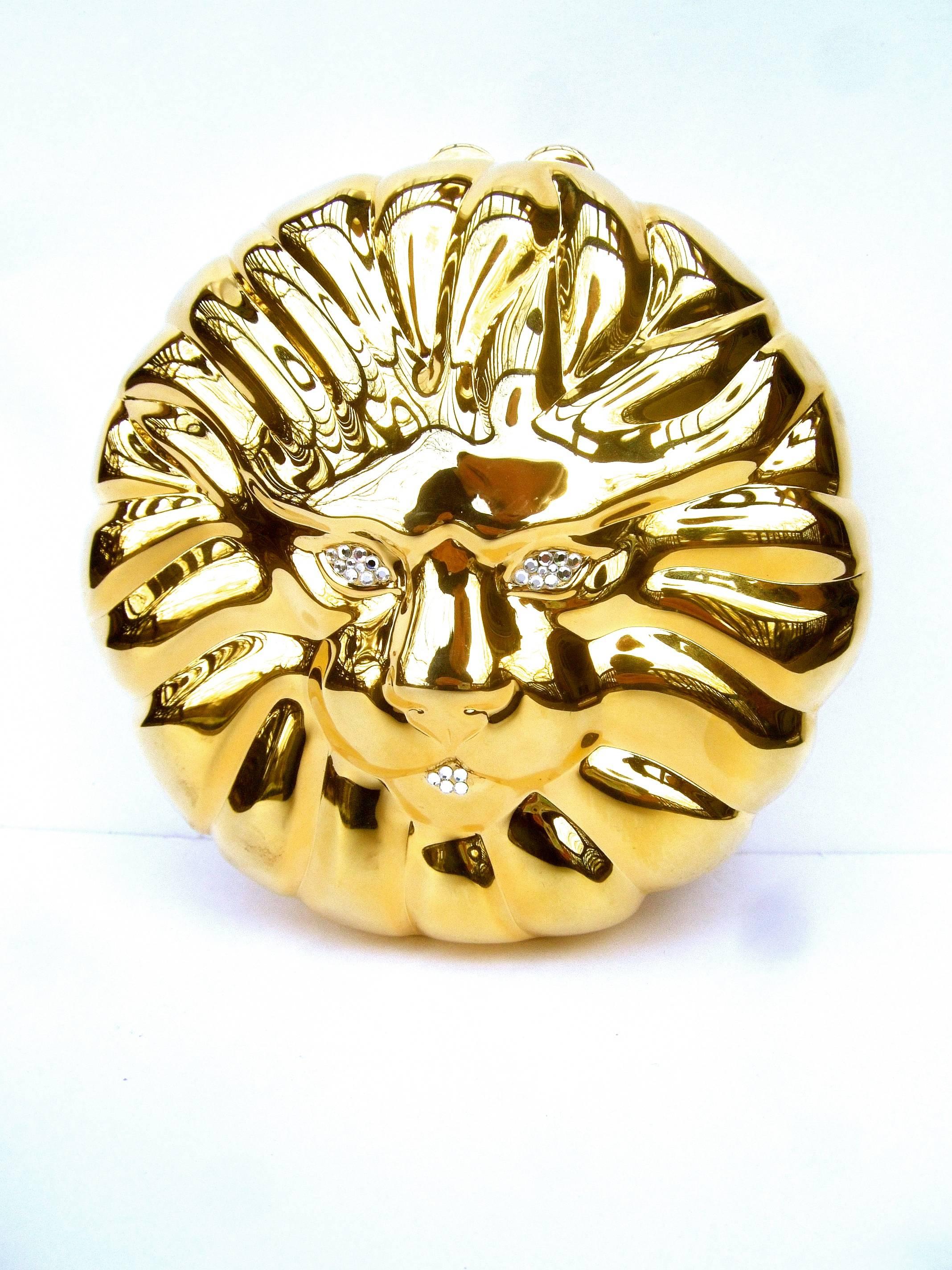 Sleek gilt metal lion face evening bag ca 1980s
The elegant evening bag is designed with a 
stylized lion's face accented with glittering  
diamante crystal eyes & mouth 

The rounded gilt metal front exterior has 
impressed ridges that emulate the