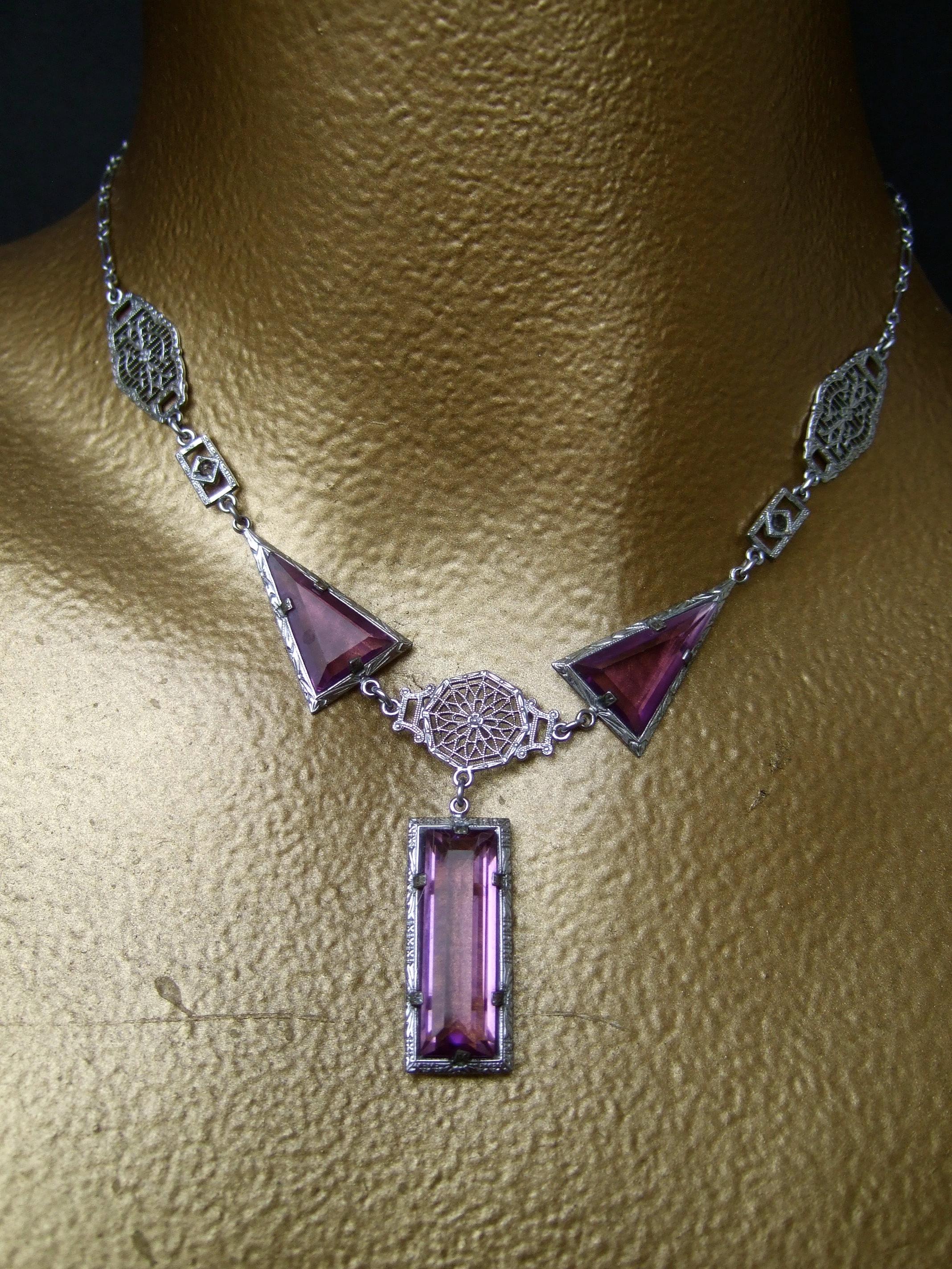 Collana e bracciale in cristallo di ametista Art Deco opulento degli anni '30 
L'elegante set è impreziosito da cristalli di vetro geometrici color ametista. 
In delicato metallo color argento con accenti in filigrana 

Il raffinato set ha un design