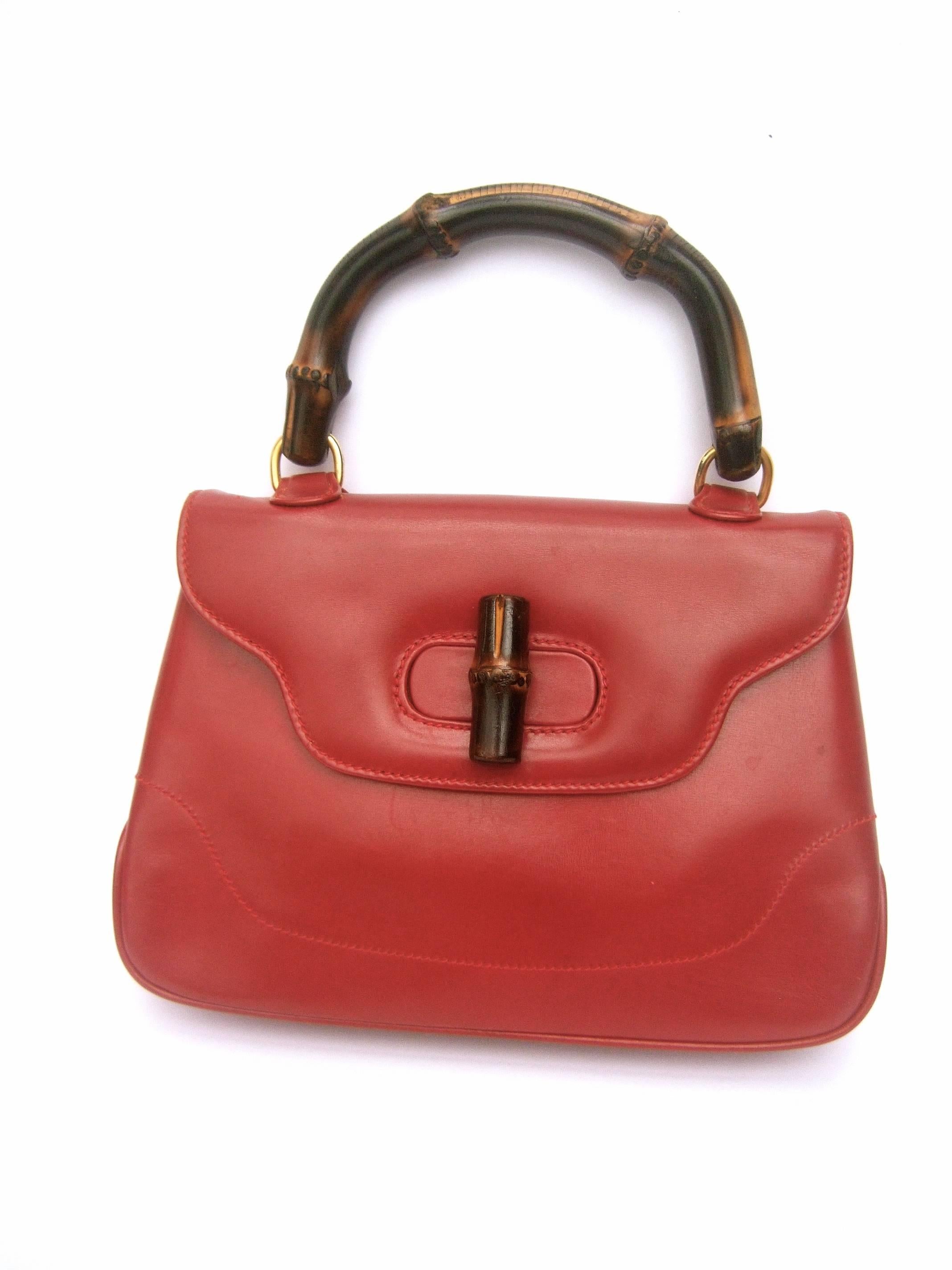 Gucci Italy Iconic cherry red leather bamboo handbag in box c 1970
The classic Gucci handbag is designed with their
signature bamboo wood handle and matching toggle
clasp. The swiveling wood handle is anchored with 
a pair of gilt metal jump rings