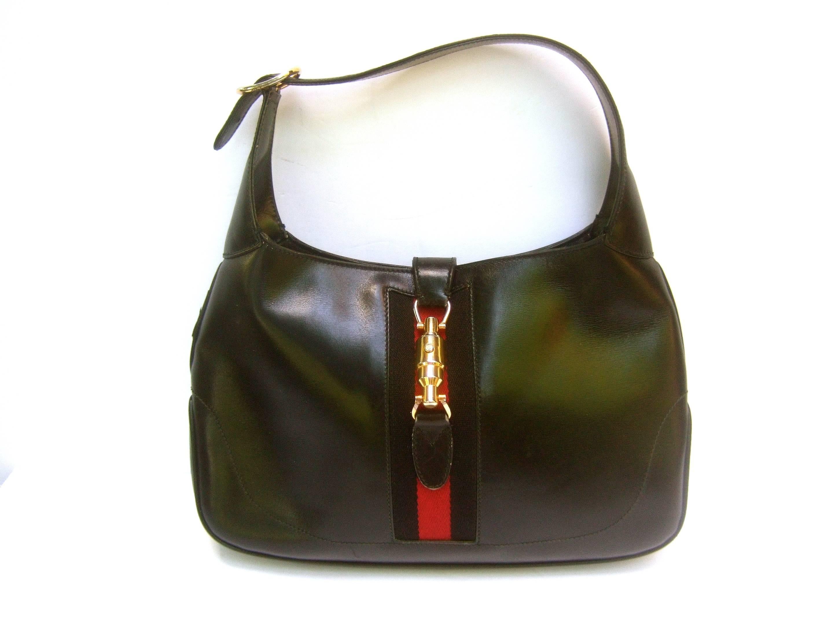 Gucci Italy Iconic black leather piston Jackie O handbag ca 1970s
The classic Gucci handbag is designed with ebony leather 
Accented with Gucci's signature red and black canvas 
webbed stripes

The sleek gilt metal cylinder clasp mechanism is