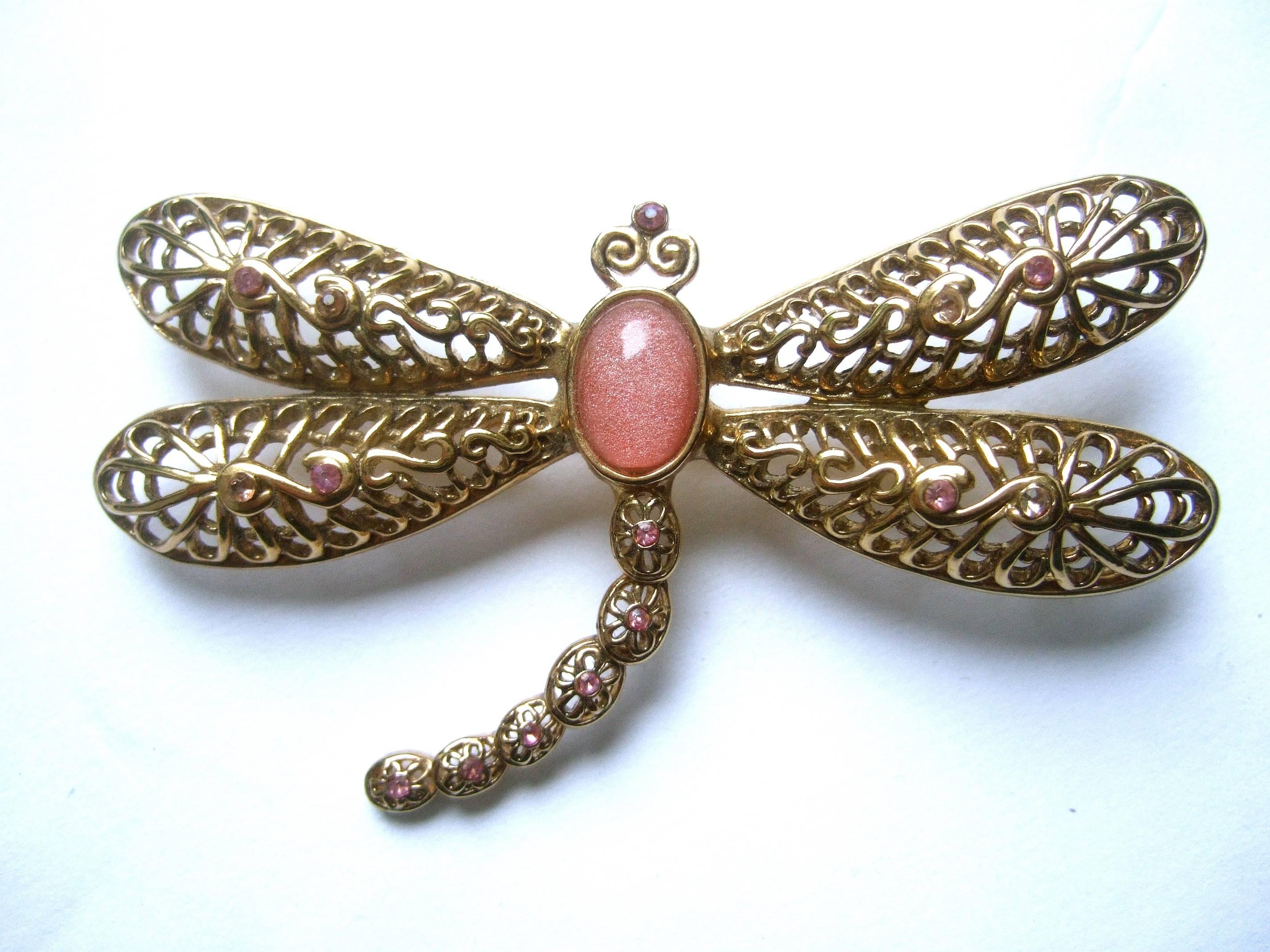 Exquisite massive crystal dragonfly brooch 
The stylized dragonfly brooch is designed 
with sinus bands of gilt metal

The wings and tail are embellished with 
tiny restrained pink crystals. The body
is adorned with a pale pink cabochon  

The