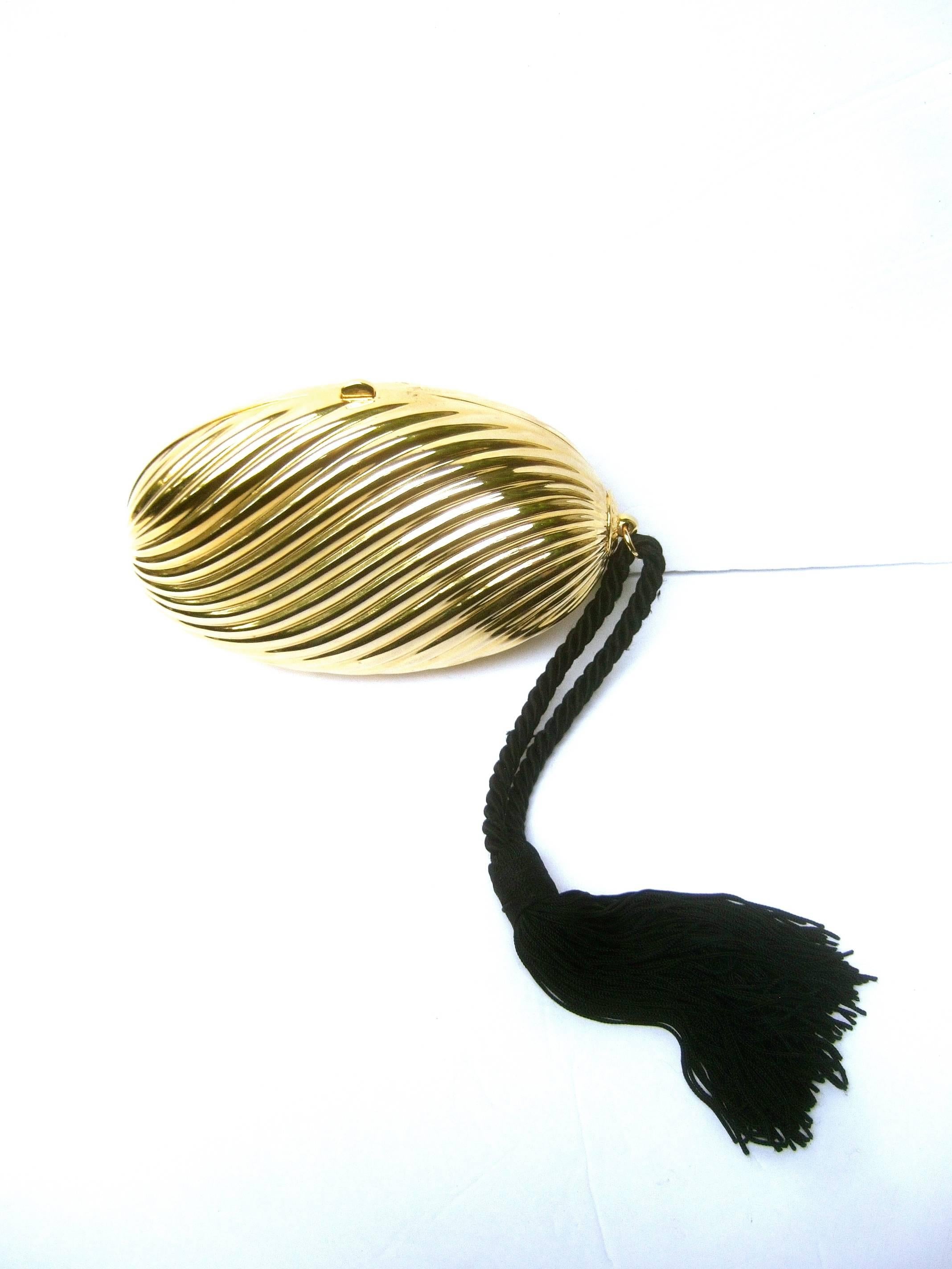 Saks Fifth Avenue Opulent Italian gilt metal evening bag c 1970s
The elegant oval shaped minaudiere is designed with sinuous 
grooved lines

Dangling from one side is a black fringe rope tassel 
The interior is lined in black felt labeled on a metal