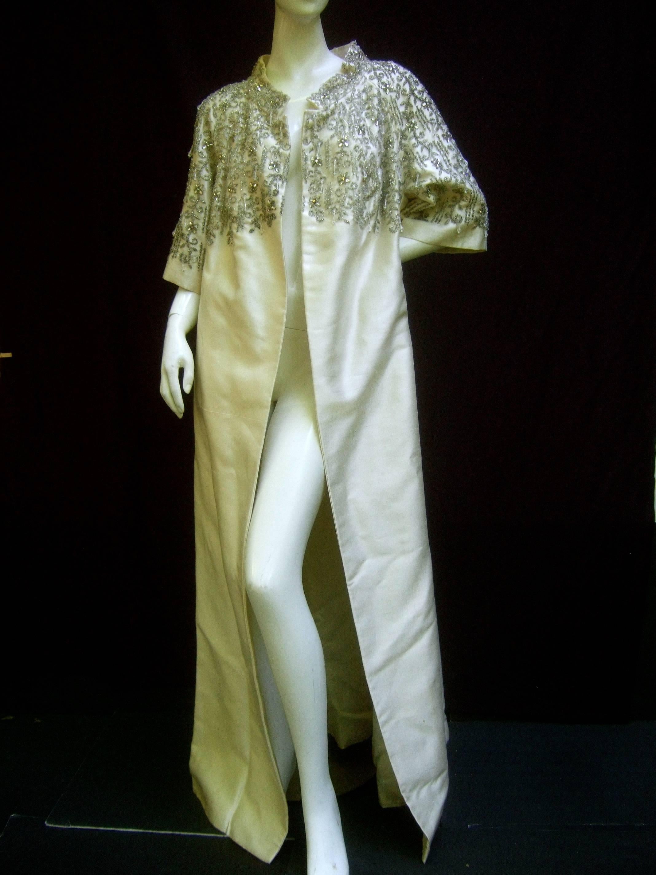 Exquisite oyster silk shantung crystal beaded opera coat c 1960
The lavish ivory silk beaded evening coat is encrusted with 
intricate clusters of glass beads and glittering crystals 

The ornate beading embellishes the bodice, Nehru collar
and