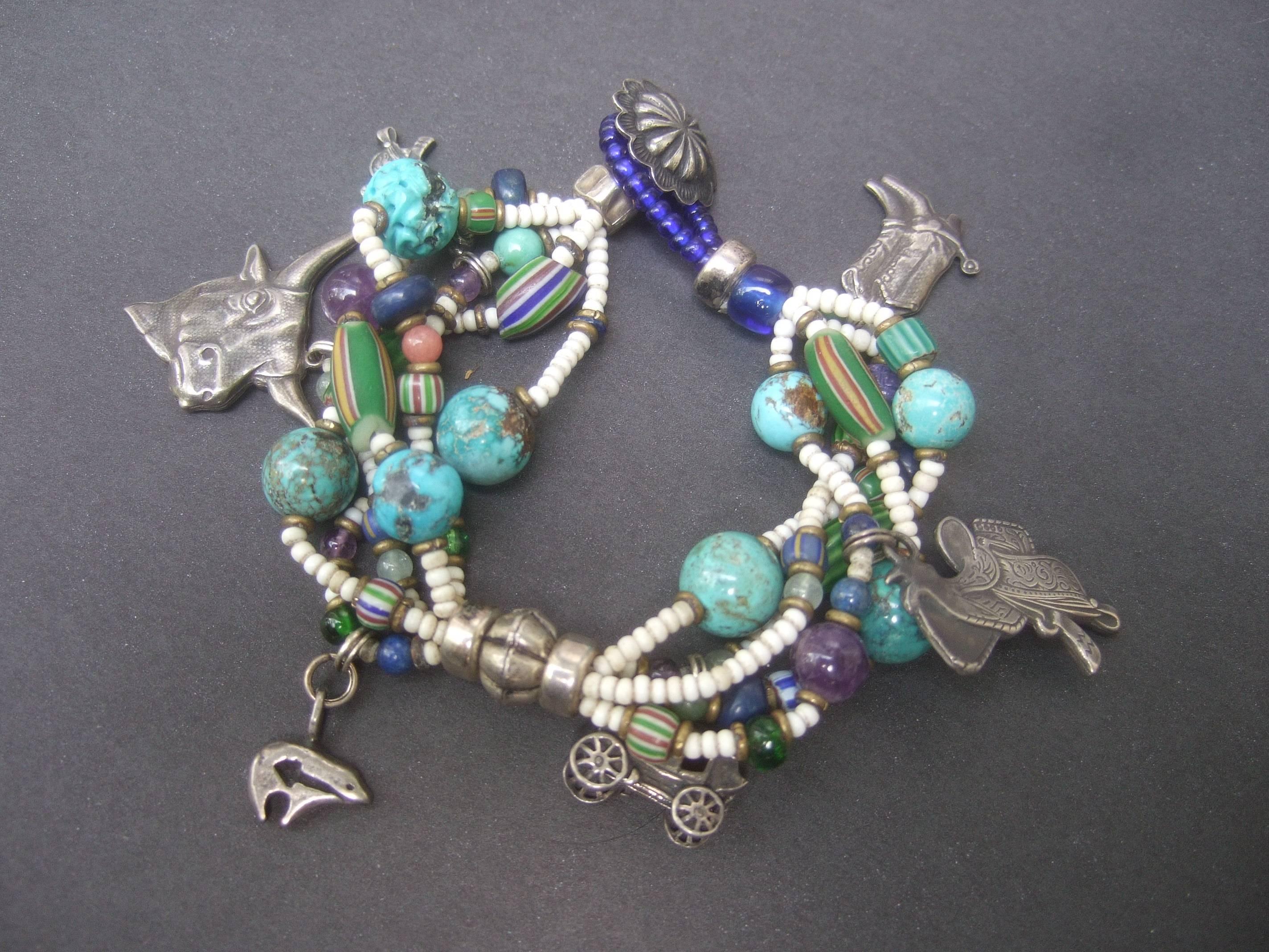 Semi precious sterling silver western theme charm bracelet ca 1980s 
The handmade artisan bracelet is designed with sporadic turquoise 
nugget beads; interspersed with amethyst and green elongated glass 
beads

Embellished with a collection of