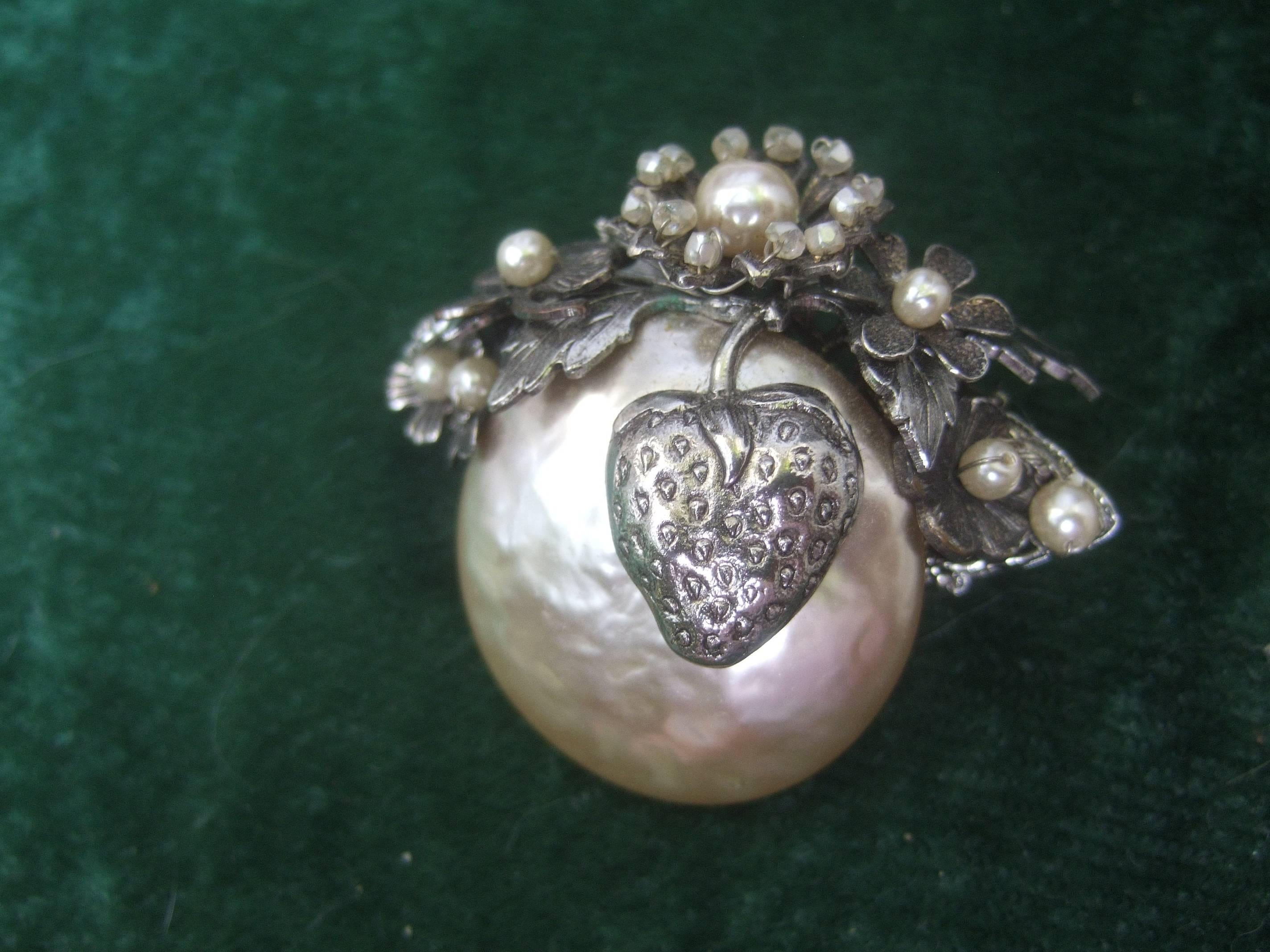 Miriam Haskell Elegant baroque glass pearl brooch ca 1950
The large glass baroque style pearl is adorned with
a silver metal tone strawberry

Designed with intricate silver metal etched leaves
with floral pedals encrusted with tint glass