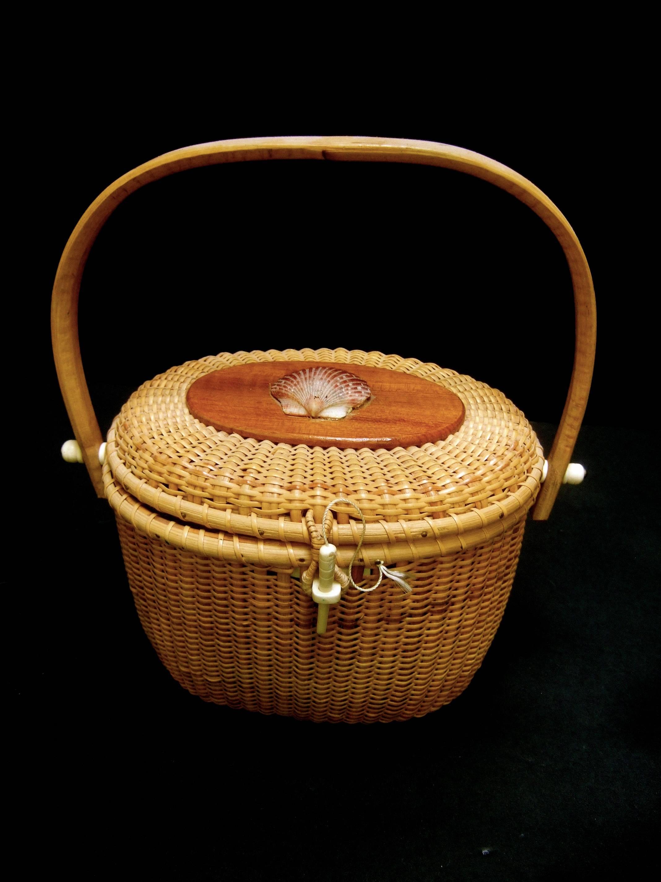Nantucket style woven wicker basket handbag 
The iconic summer handbag is adorned 
with a sea shell mounted on the oval wood
plaque lid cover

Carried with a bent wood swivel handle 
Secures with an ivory resin toggle cylinder
closure

Makes a chic