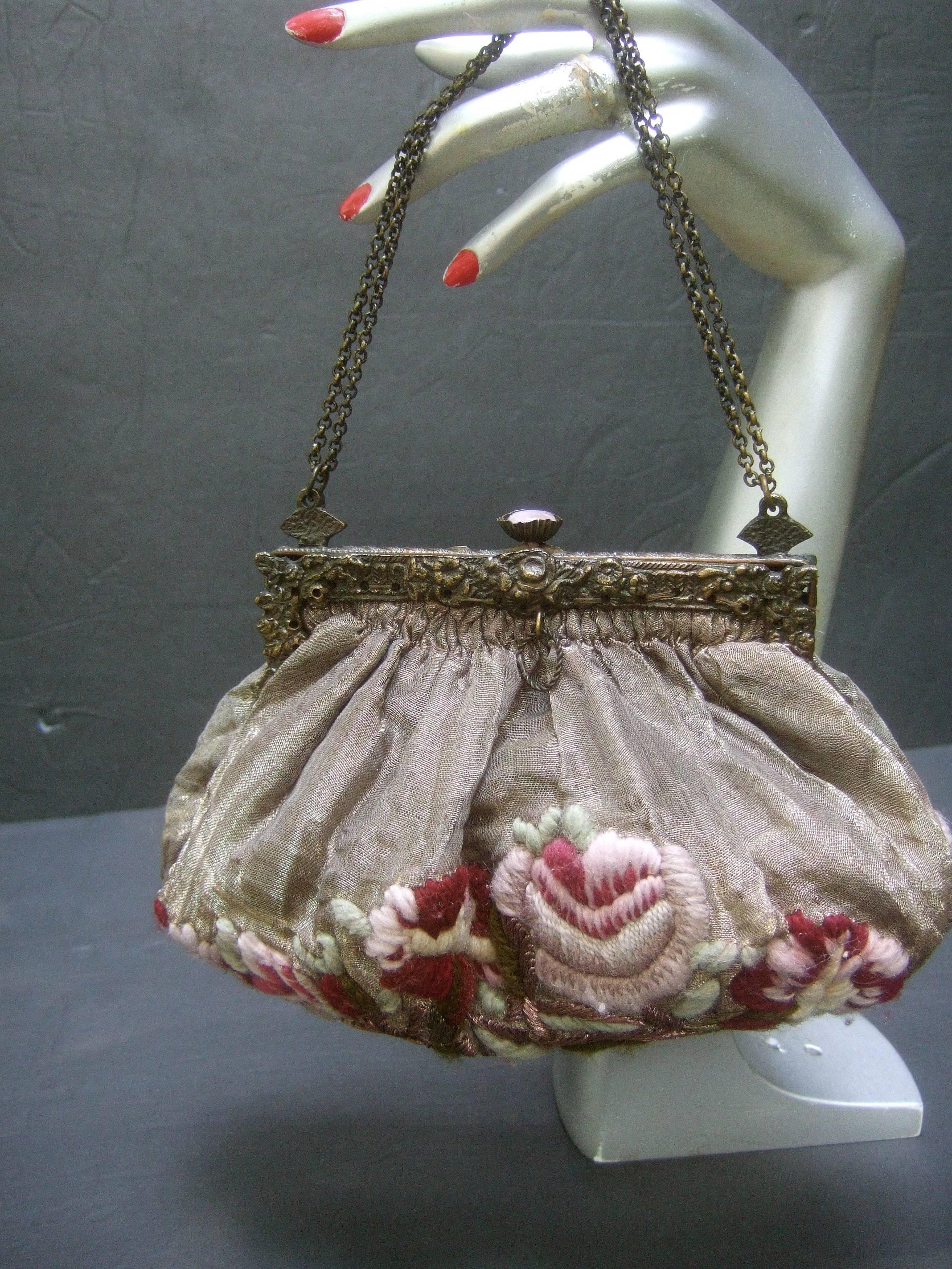 Exquisite art nouveau victorian evening bag c 1920s
The antique evening bag is covered with bronze
metallic organza embellished with mauve & magenta 
embroidered flowers on both sides 

The ornate brass metal clasp frame has an aged 
darkened
