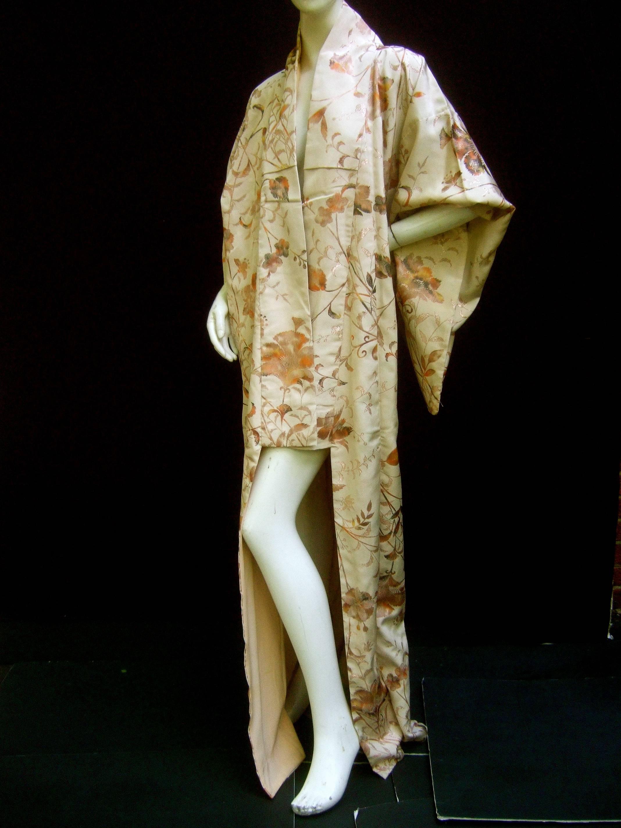Exotic Japanese floral brocade kimono c 1970s
The elegant kimono is designed with a garden 
of lush flower blooms in autumn hues 

The background is beige sand color that illuminates
the brown and burnt orange blooms. The sinuous leaves
are accented