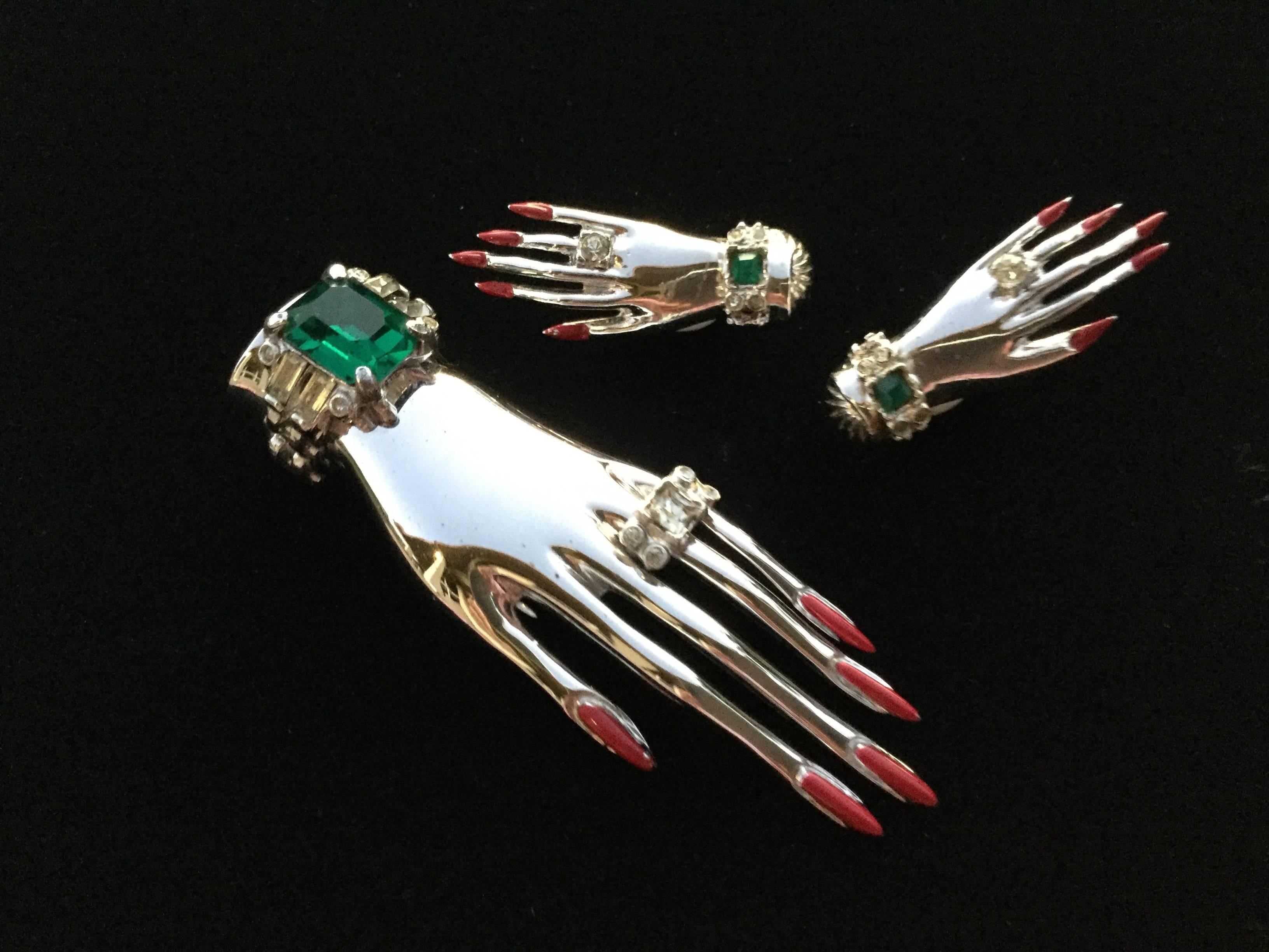 Intriguing Corocraft Sterling silver clip and earring set depicting carefully manicured hands. Wonderful large emerald green square cut paste. Bright red enameled fingernails.  Each piece of this set is a miniature sculpture.  Excellent Condition.