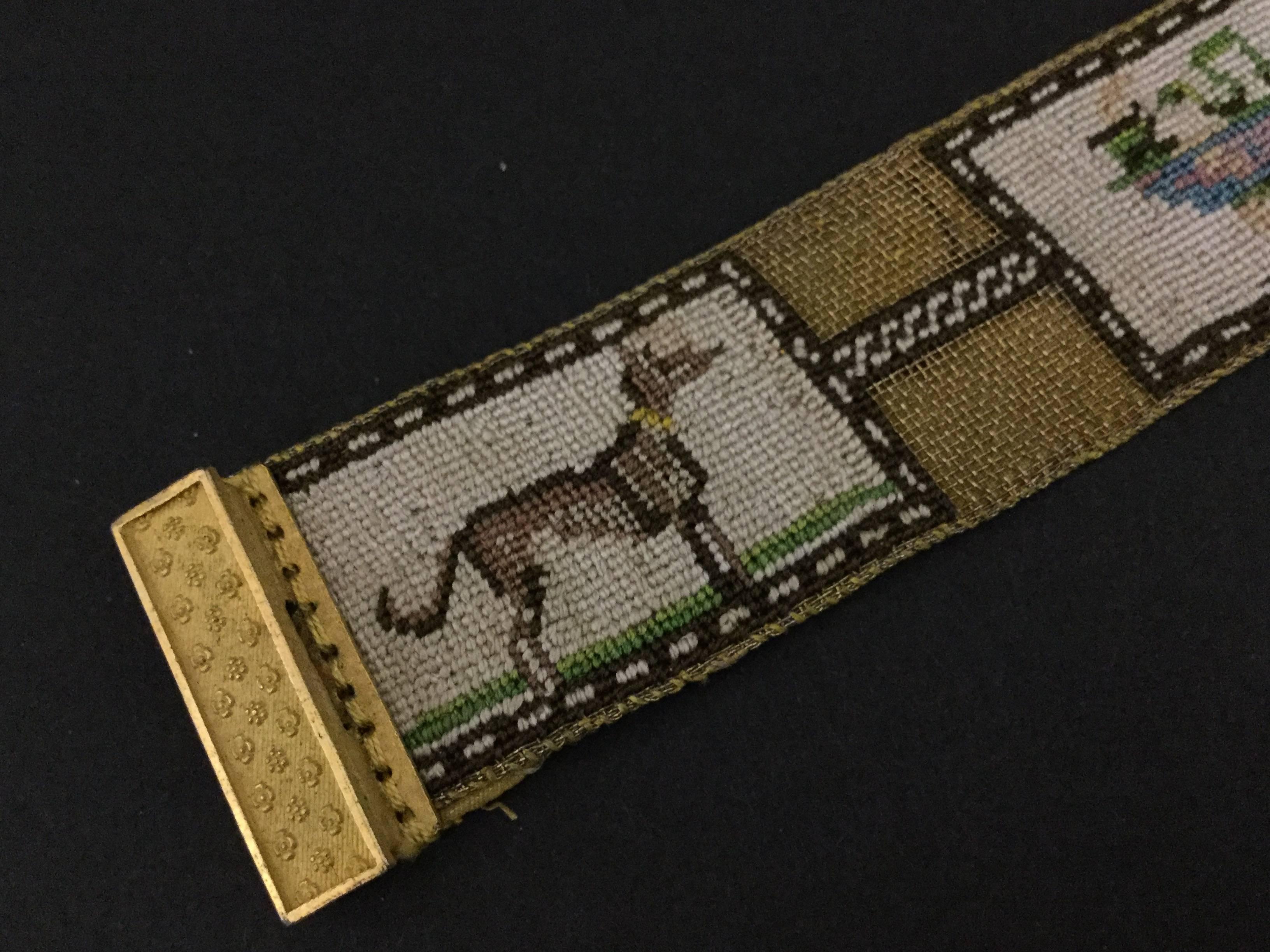 This bracelet features three oblong panels of super fine embroidery set on a metallic gold netted backing which is lined on the reverse with gold silk. This fastens with a pinchbeck clasp decorated with an embossed star pattern.
The panels depict a