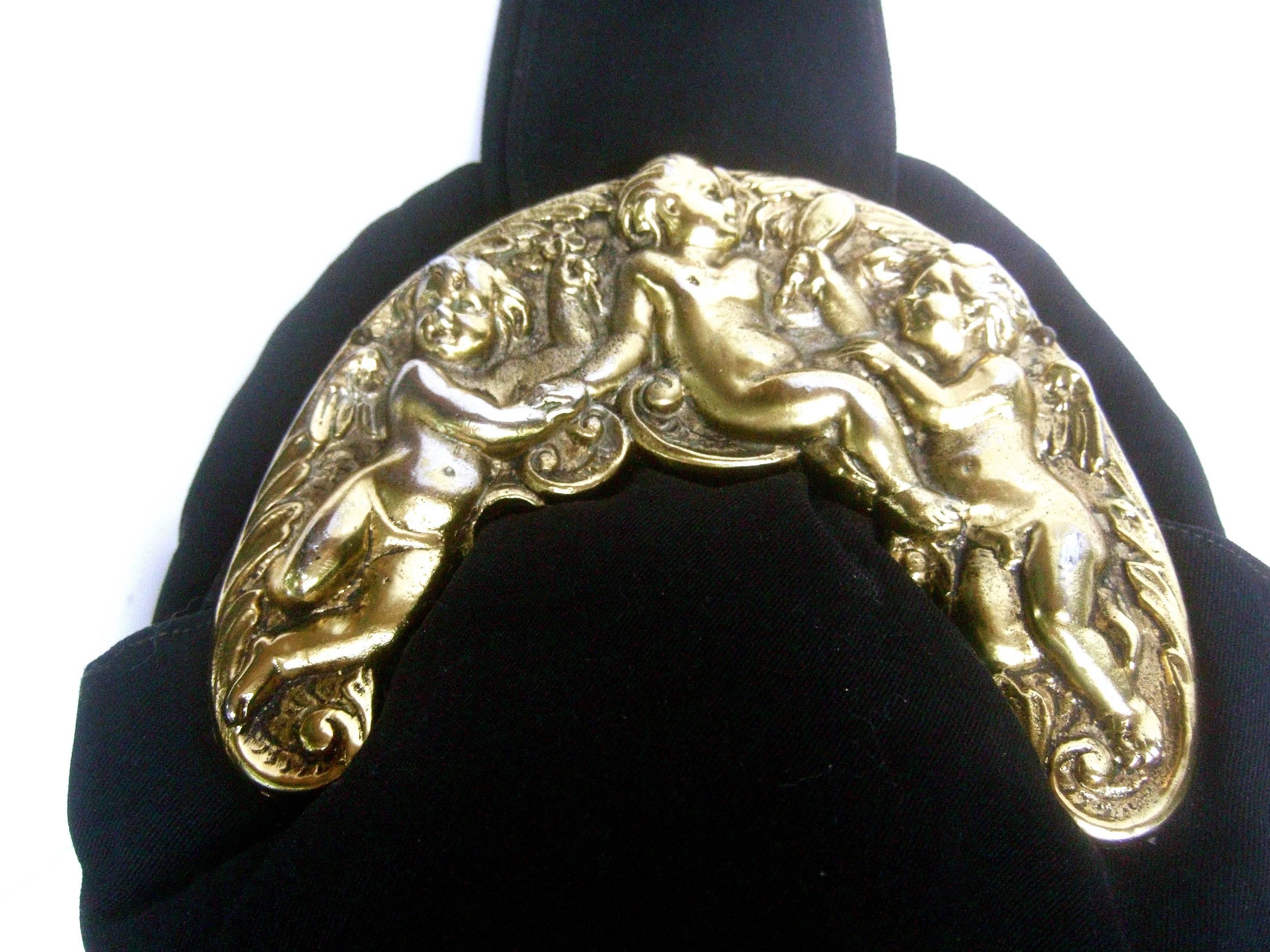 Ornate brass metal cherub emblem black cloth evening bag c 1950s 
The elegant midcentury evening bag is adorned with a
brass repousse plaque with a pair of winged cherubs 
and a young nude woman gazing into a vanity mirror 

The black cloth handle