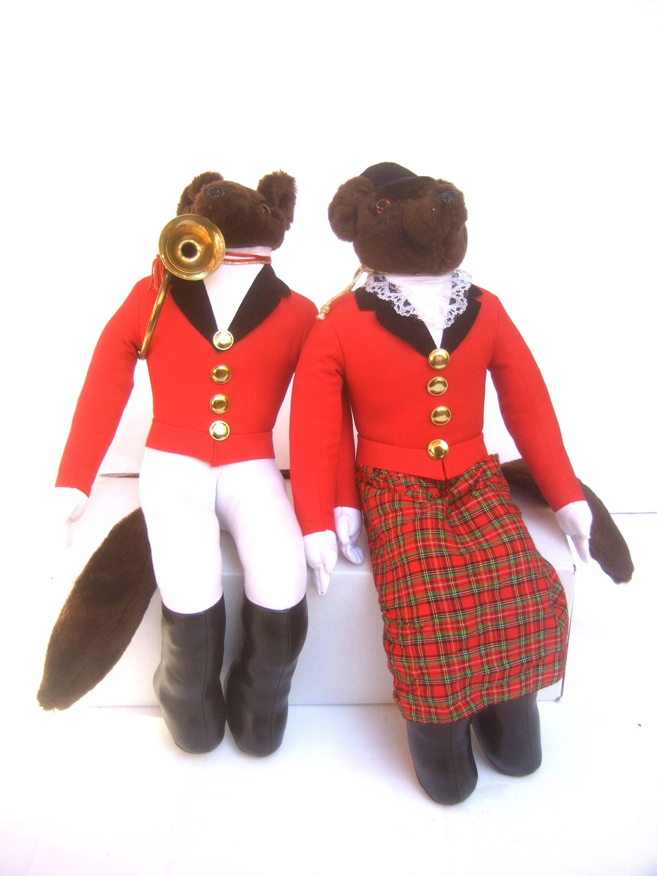 Whimsical pair of fox hunting stuffed figures c 1980s 
The charming pair of foxes are dressed in English
style equestrian hunting attire 

The male fox is dressed in a red hunt  
jacket with gilt metal buttons. Paired with 
the requisite brass horn