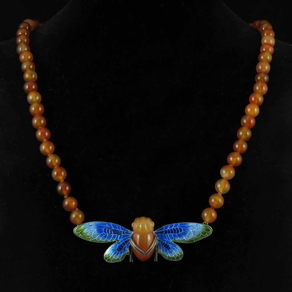 This gorgeous Art Deco era Chinese export necklace features an elaborately carved carnelian cicada with enameled wings that look like stained glass. The cicada is deeply carved and very three dimensional. The radiating wings are enameled in subtle