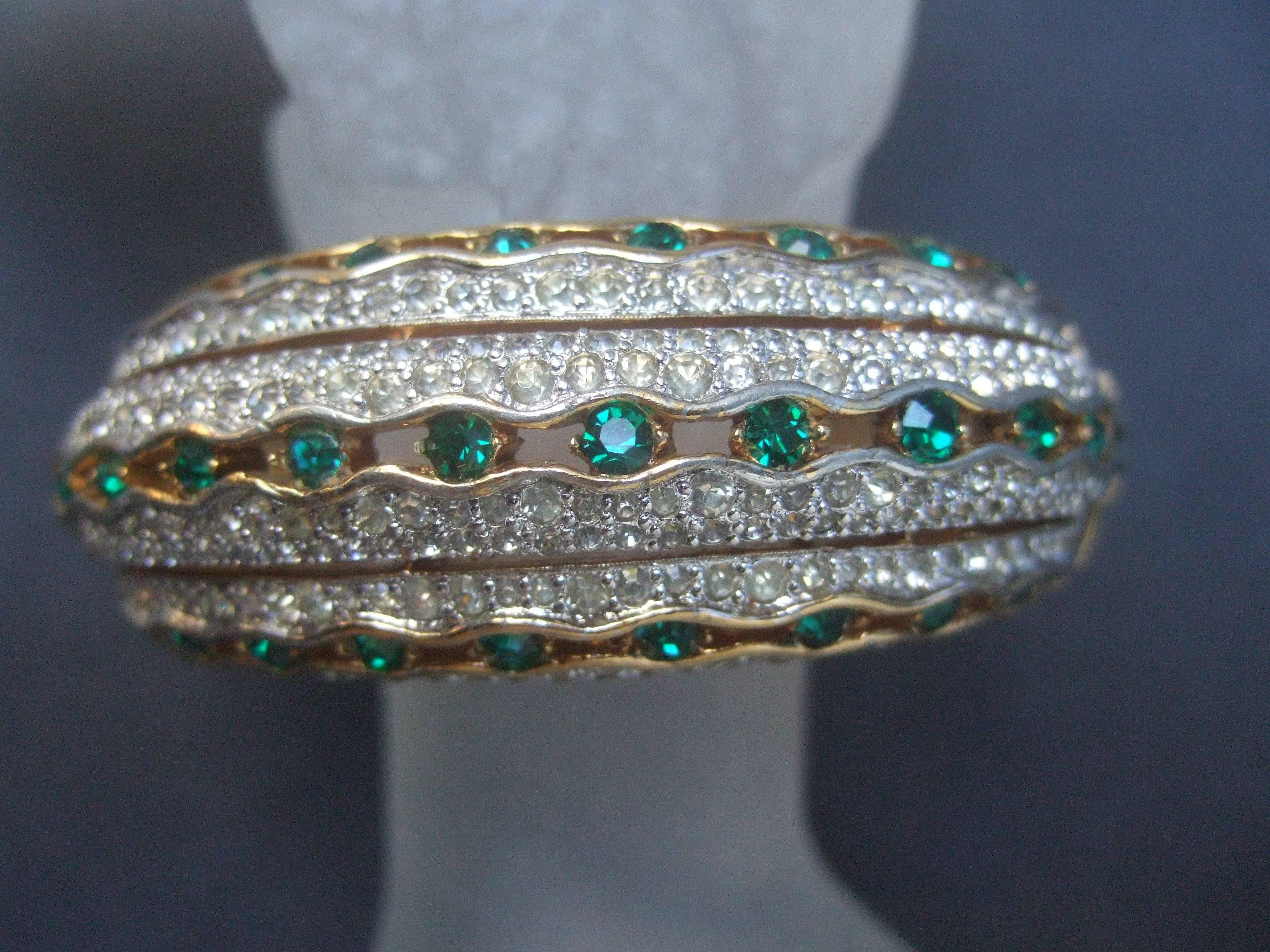 Jomaz Crystal encrusted wide gilt metal hinged bangle c 1970
The exquisite bracelet is designed with three bands 
of emerald green color crystals 

Embellished with six sections of contiguous pave crystals 
Joseph Mazer was one of the preeminent