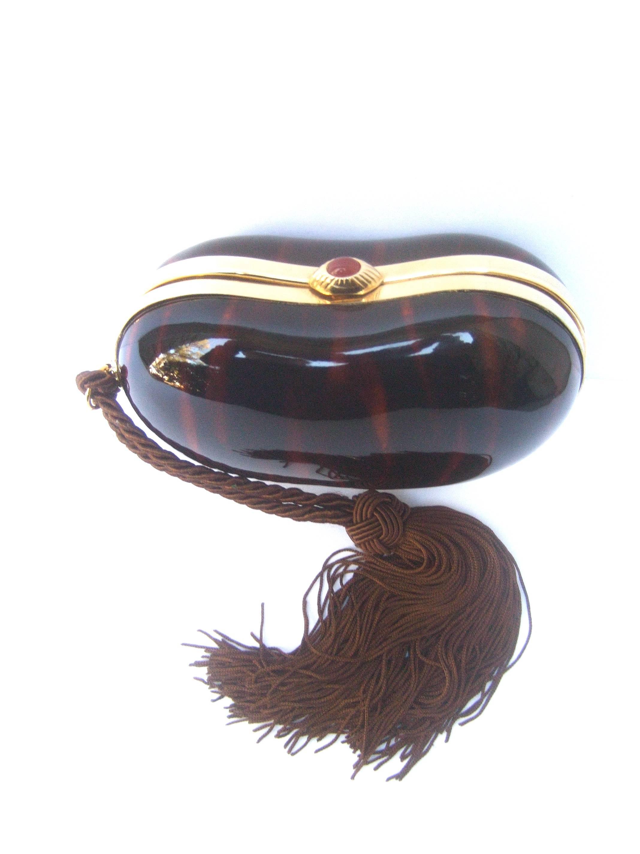 Saks Fifth Avenue Italian tortoise shell lucite tassel evening bag c 1970s
The elegant kidney shaped lucite clutch bag us framed with sleek
gilt metal trim that circles the opening 

Dangling from one side is a braided brown fringe tassel. The gilt