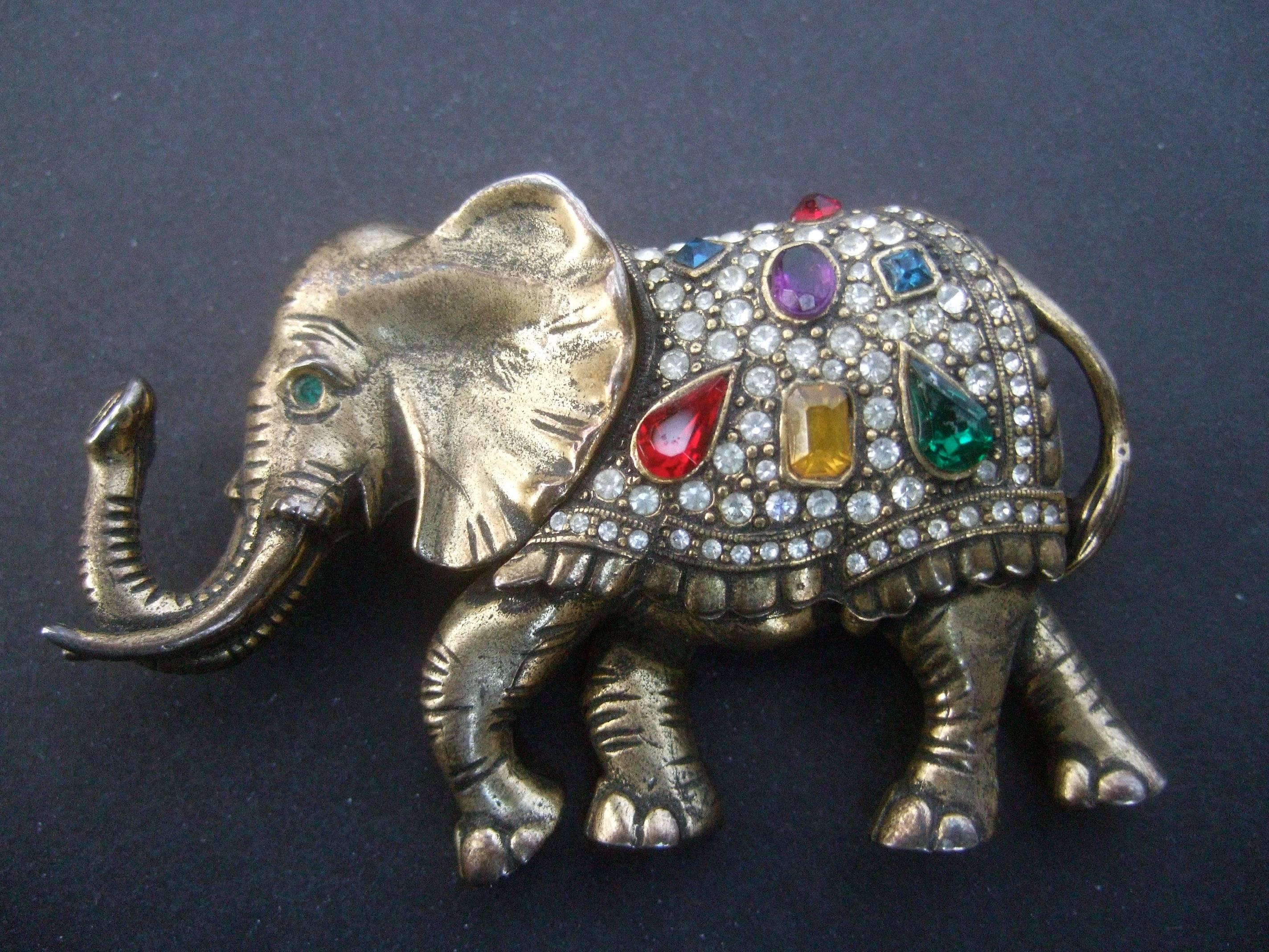 Jeweled crystal brass metal elephant brooch c 1970s
The majestic brass metal elephant brooch is encrusted 
with a collection of jewel tone crystals 

The jewel tone crystals are juxtaposed with a series 
of glittering clear pave crystals. The brass