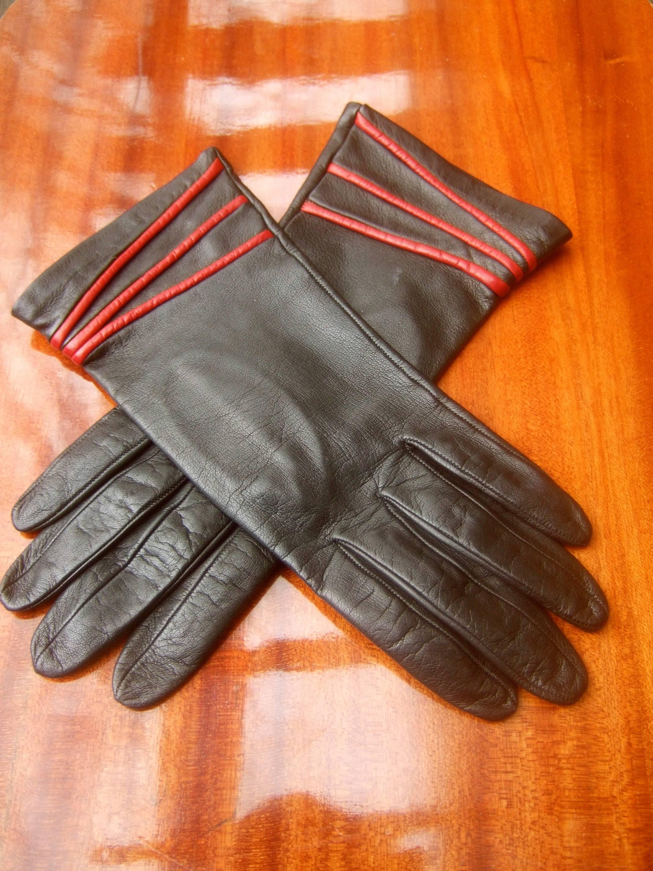 Yves Saint Laurent Italian ebony leather driving gloves c 1980s 
The stylish Italian gloves are designed supple black leather 
The ends at the opening are accented with a trio of red leather bands 
The interior is lined in black silk labeled Yves