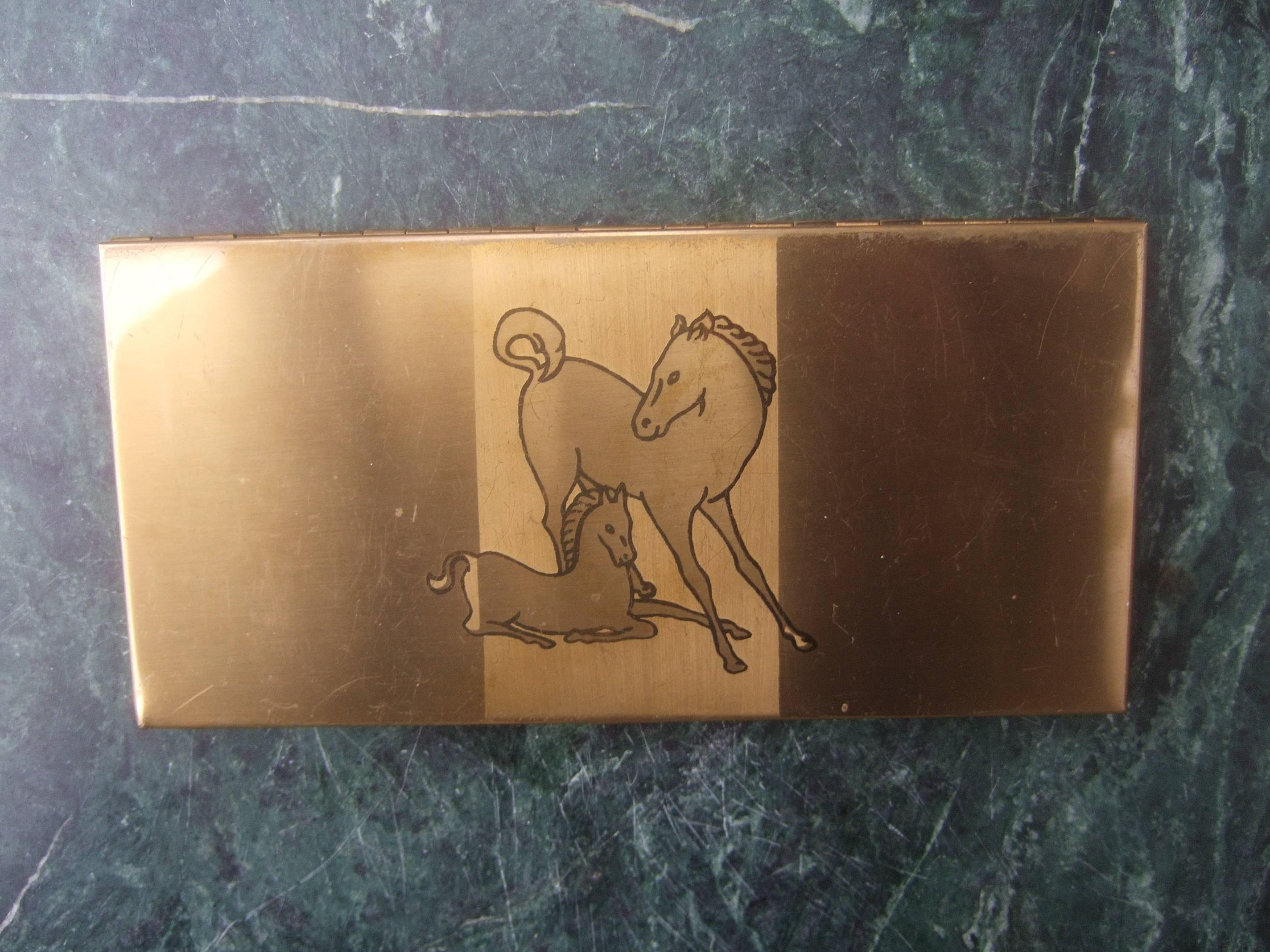 Mid-century brass metal equine cigarette case c 1960
The stylish retro cigarette case is designed with a horse
and colt offspring on the lid cover

The pair of equine are illuminated in silhouette against
a brushed satin brass metal background 
The