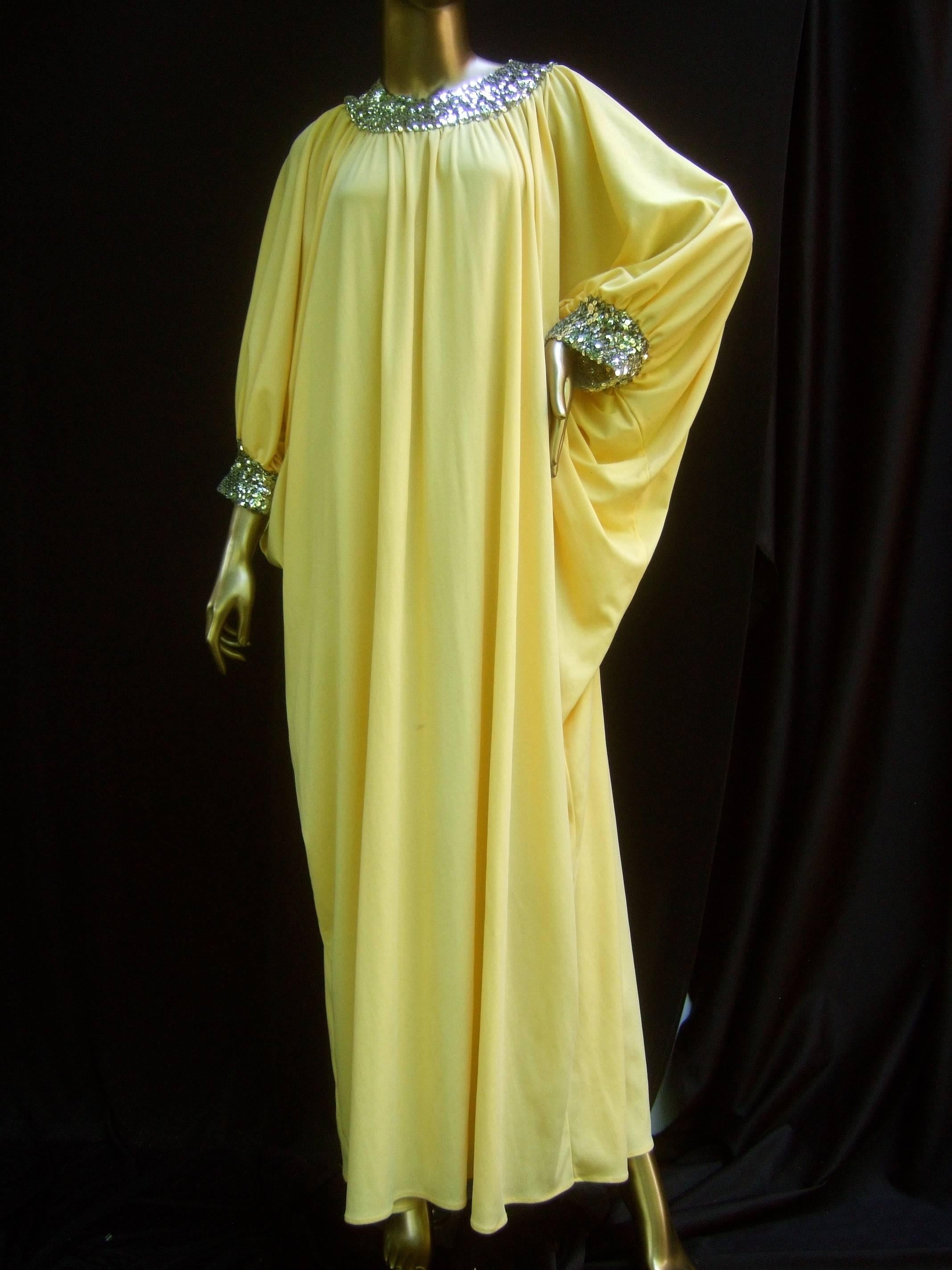 1970s Saks Fifth Avenue lemon yellow poly knit caftan gown 
The stylish polyester caftan lounge gown is designed with a 
voluminous draped silhouette and batwing style sleeves 

The collar and cuffs are framed with silver metallic sequins 
Designed