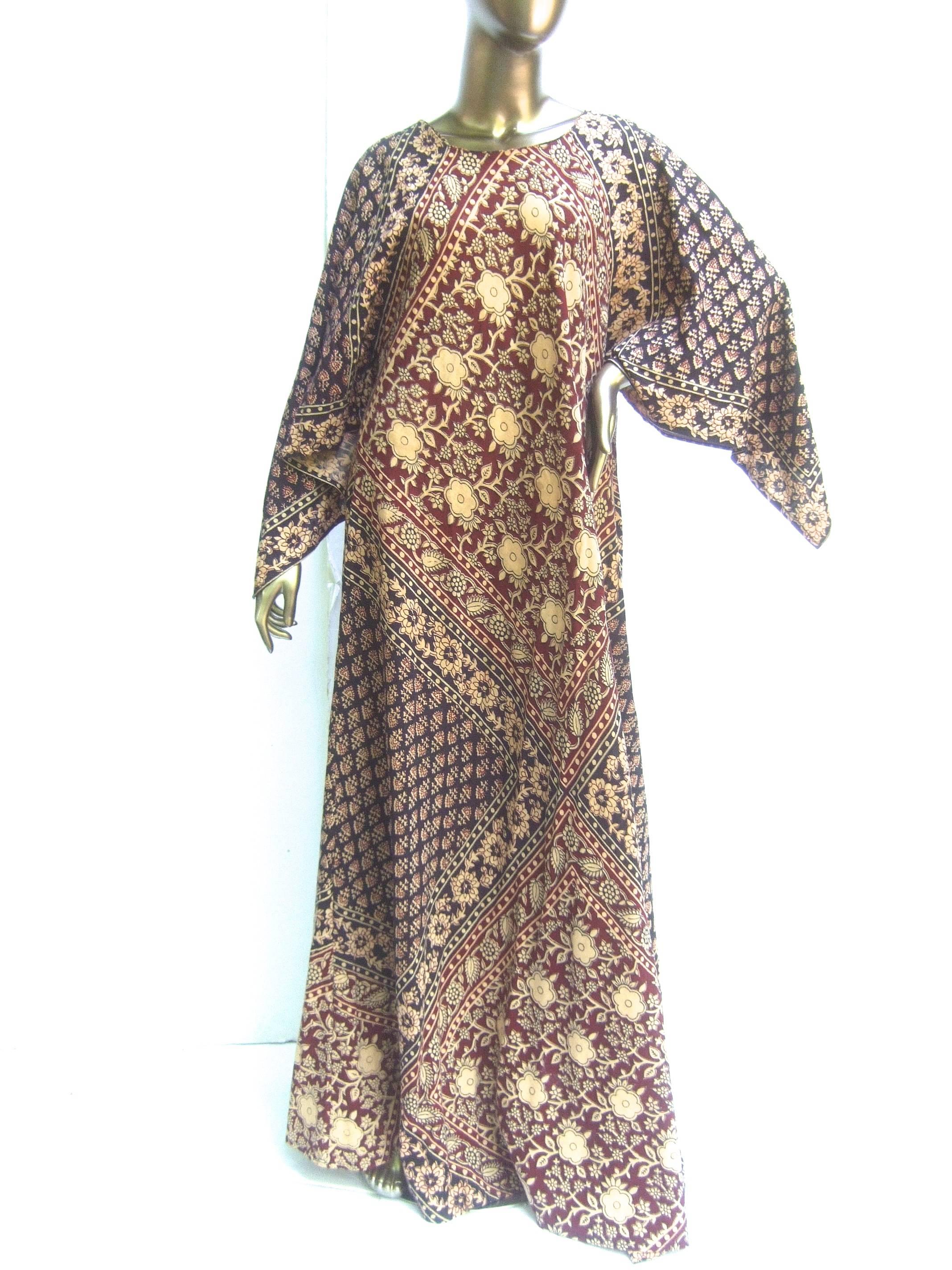 Exotic bohemian cotton print festival caftan gown c 1970s 
The ethnic caftan gown is a collage of intricate 
floral color block designs in contrasting burgundy,
beige and black 

The sleeves have a voluminous winged design 
Transitions effortlessly