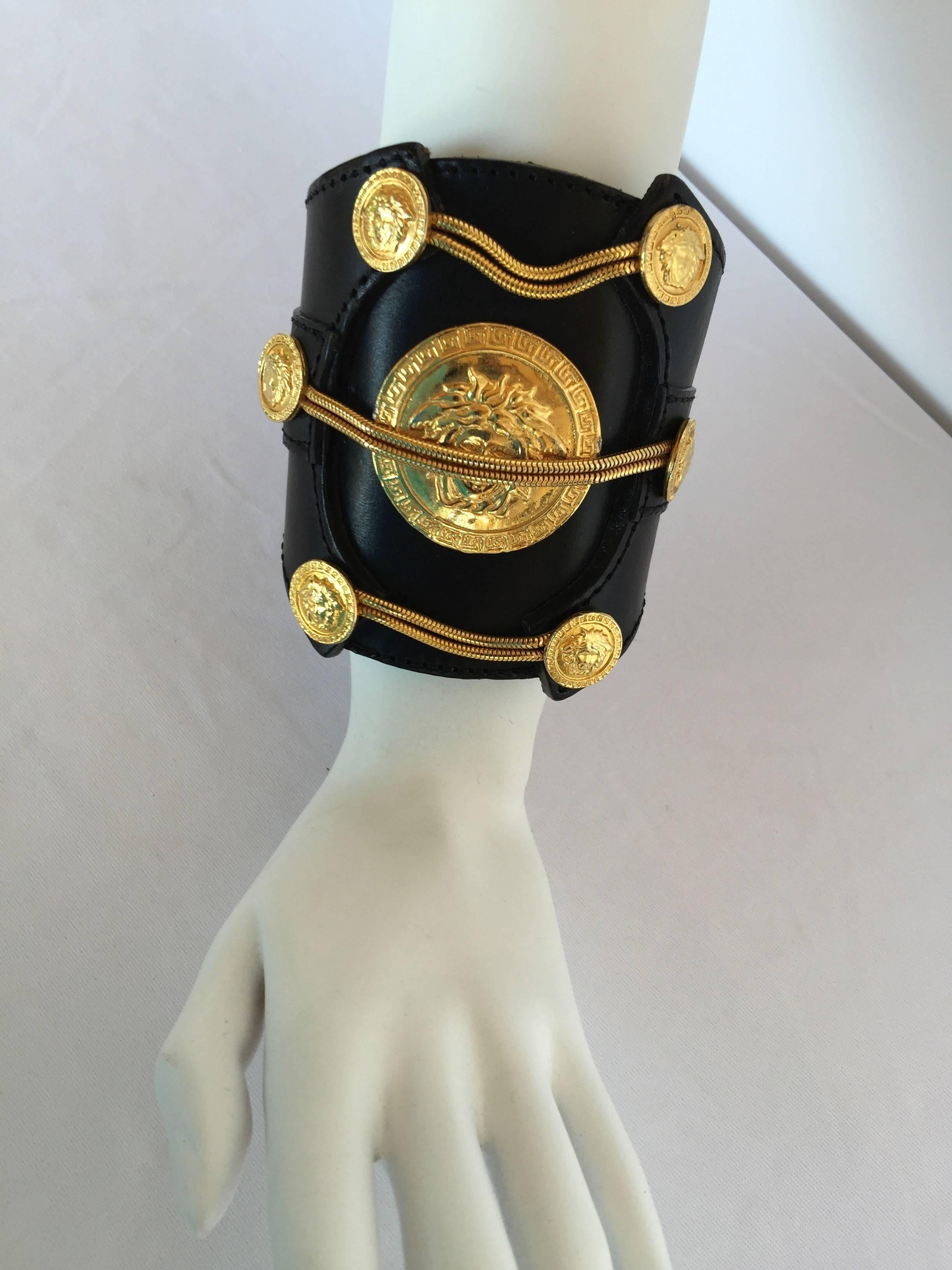 Haute couture, runway scale, black leather cuff studded with snake chains and multiple gilt Medusa medallions by Gianni Versace.

Curiously, the central Medusa's eyes are veiled by a pair of gilt chains, perhaps as a reference to the Greek idea