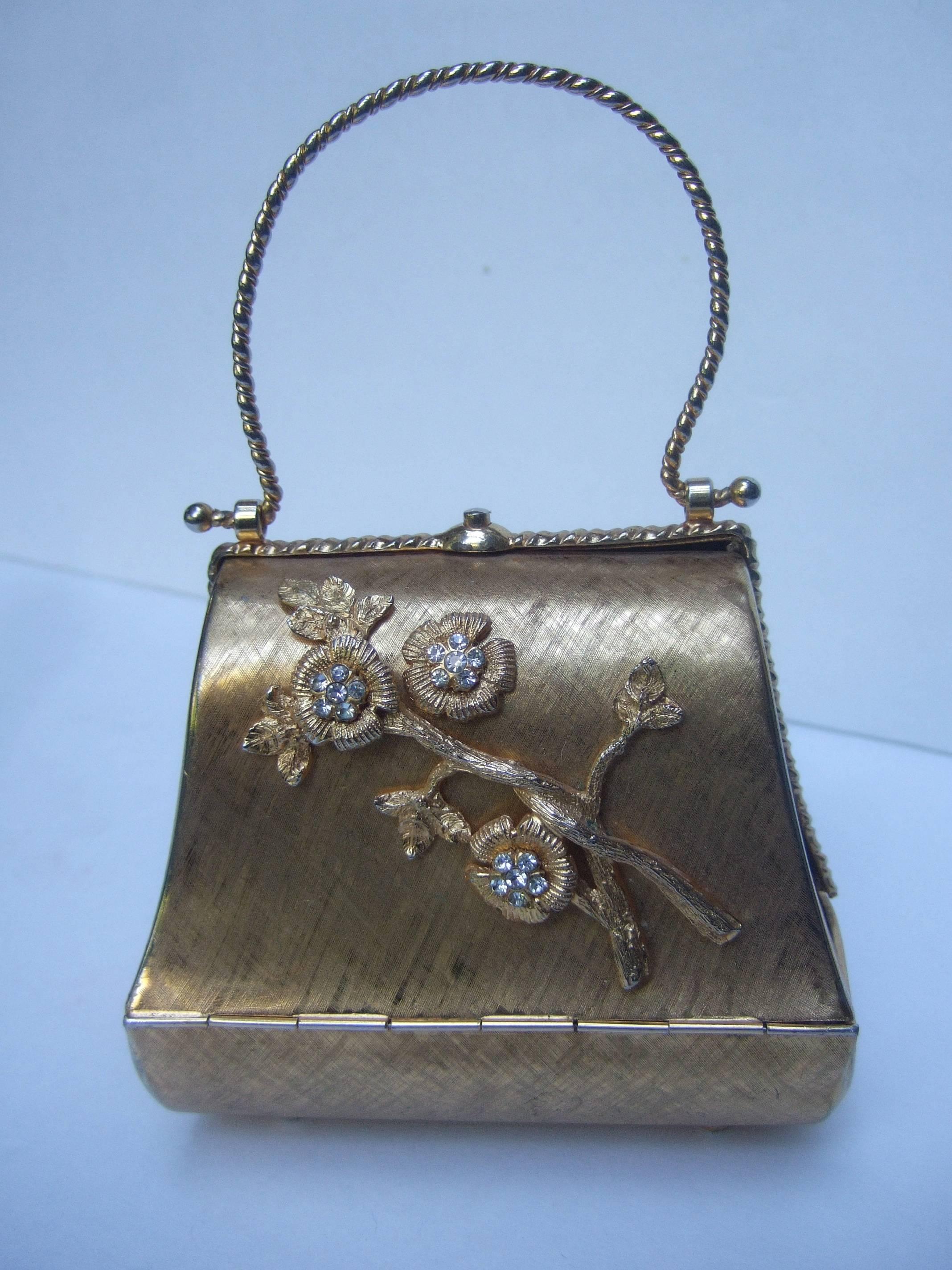 Opulent gilt metal jeweled flower evening bag c 1970
The elegant diminutive gold metal minaudiare  
purse is decorated with a branch of diamante 
crystal encrusted flowers

The small evening bag is carried with 
a gold braided metal swivel