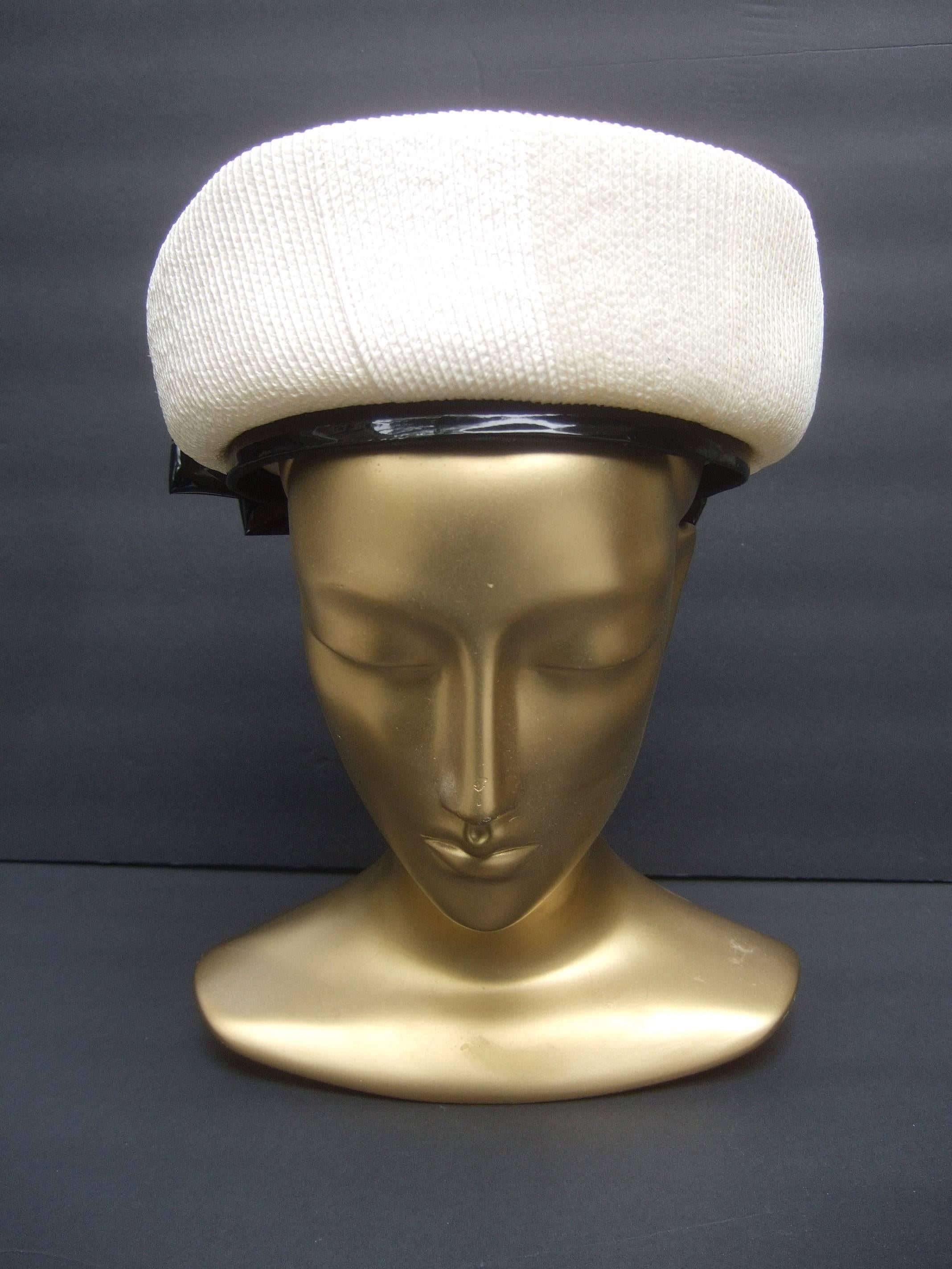 Lilly Dache Parisian style bow trim hat c 1970
The stylish retro had is designed with off white raffia
accented with a large black patent leather bow on the
back side

The interior brim of the hat is framed with a patent
leather band that