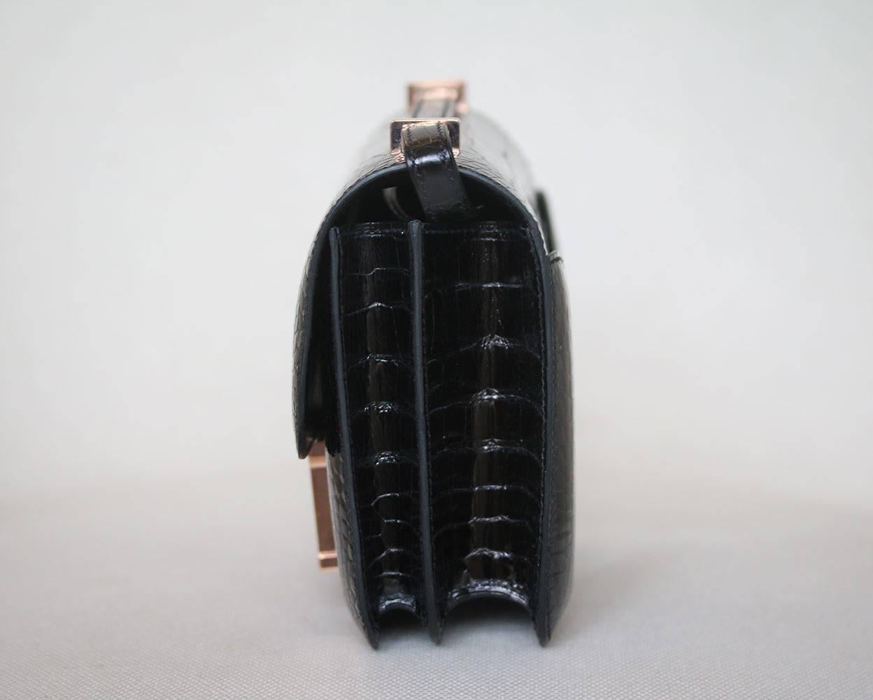 Black crocodile leather exterior trimmed with shining rose gold hardware. Lift latch single flap style closure opens to a black leather lined interior that holds 2 slit and 1 zippered side pockets. This piece is brand new. The Hermes Constance is