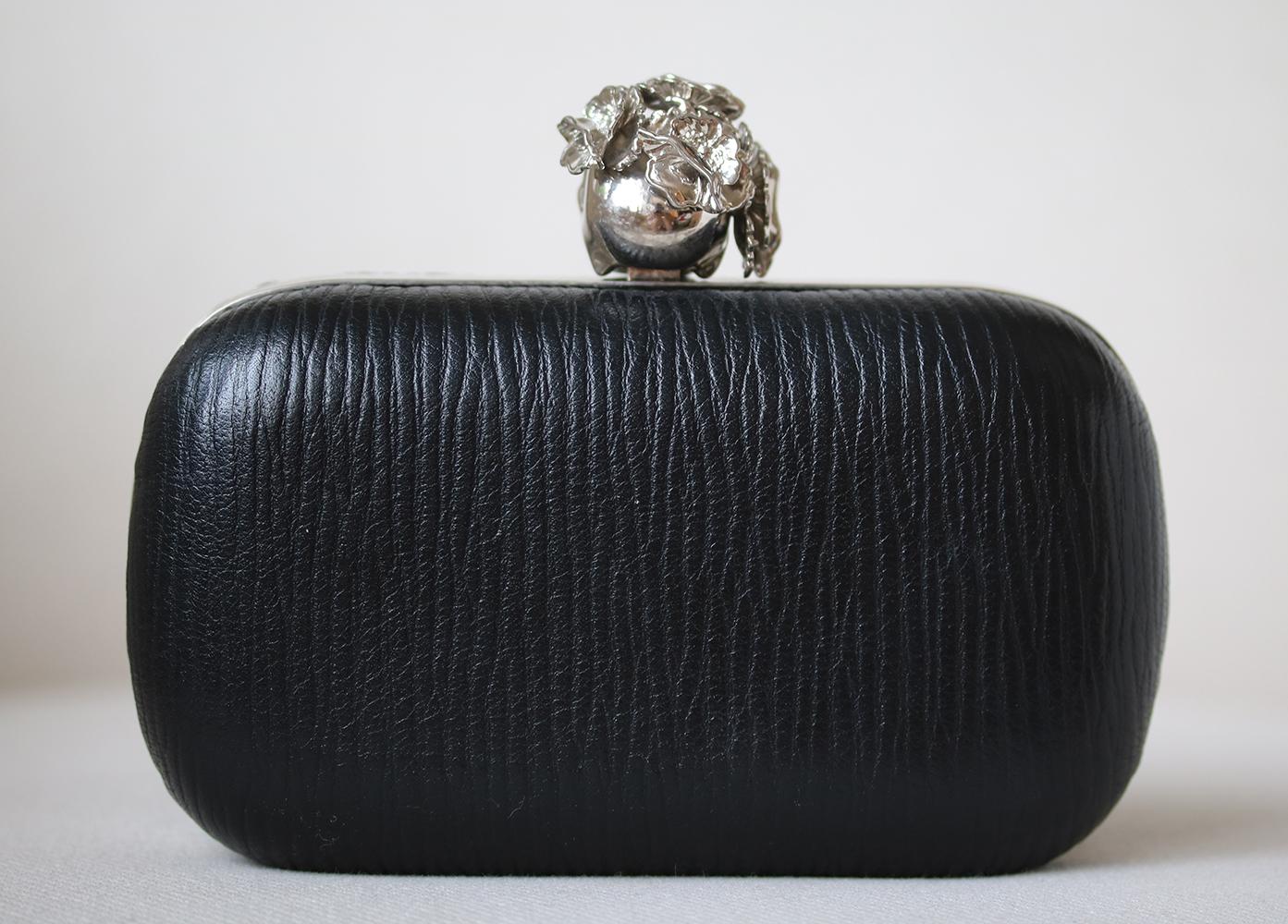 Make a statement with this bold Alexander McQueen Black Textured Leather Poppy Skull Box Clutch Bag. Featuring box frame silhouette, this clutch is covered in gorgeous black grained leather. The clutch closes with a silvertone metal and Poppy