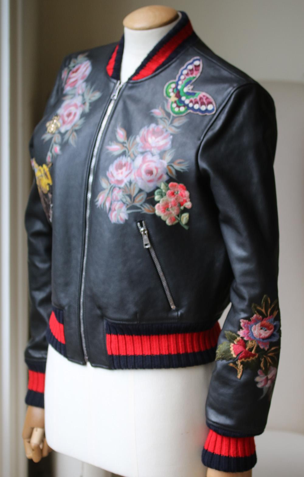 Alessandro Michele's instantly recognizable motifs adorn this editor-approved bomber jacket from Gucci. Leave an unforgettable impression. The black leather is contrasted with red and black detailing at the collar and hem, while the appliqued hand