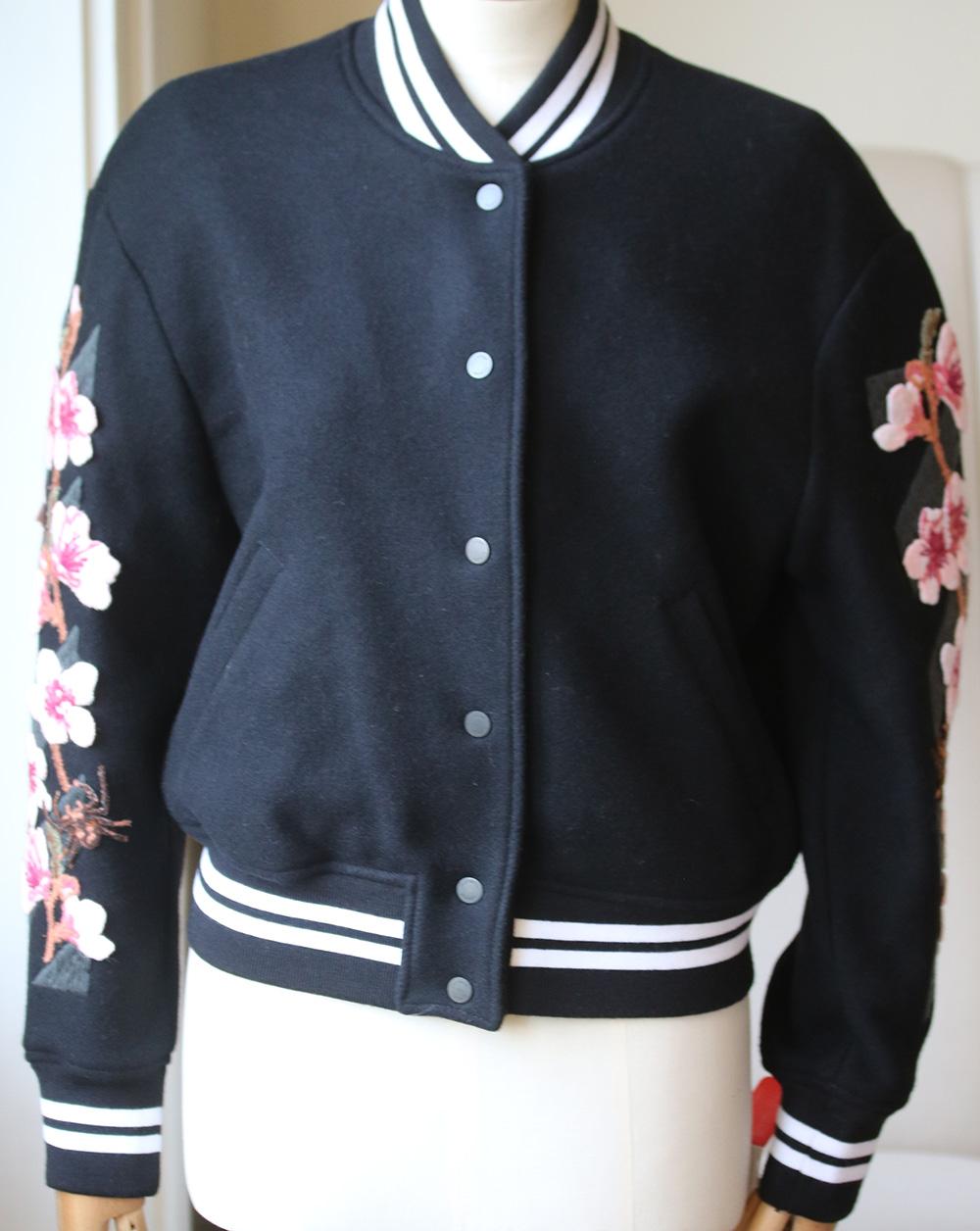 Designed in Italy, this jacket has been fabricated from a wool blend and features a mock neck, front popper button closure, long sleeves, two side pockets, black and white striped edges and a multi-coloured floral and logo embroidery at the back.