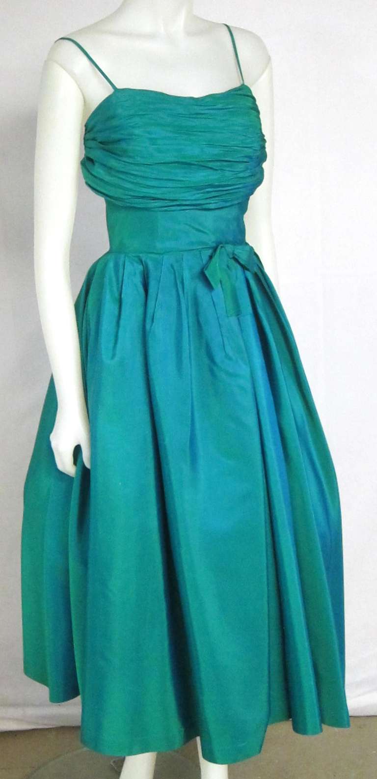 Gorgeous dress from the 1950s. Shimmering Jewel Tone Taffeta material with ruched bodice and boning, spaghetti straps, bow at waist and side metal zipper.

Bust:  32