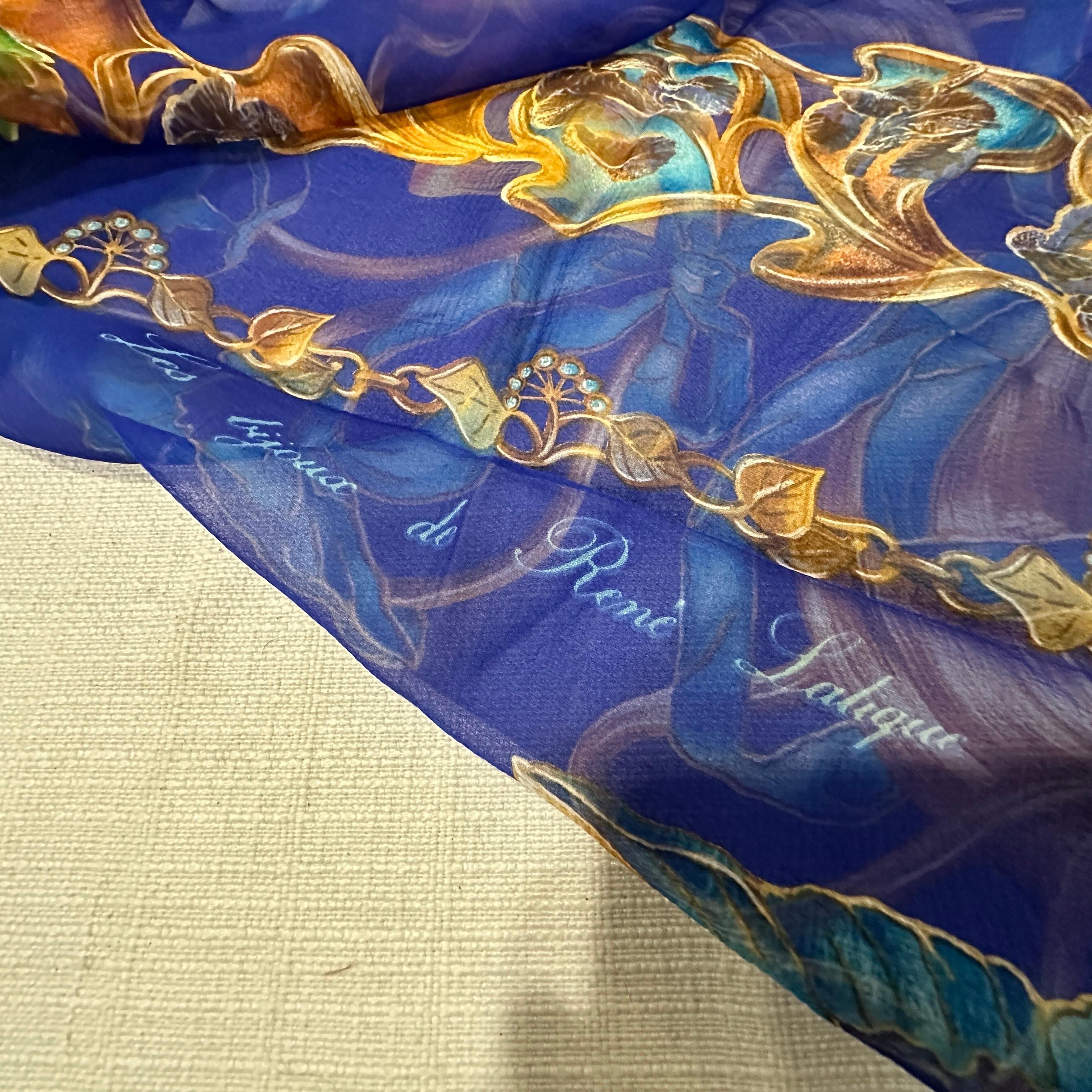 Este es un exquisito pañuelo de seda de Lalique, con un fondo azul intenso. El diseño es muy ornamentado y artístico, característico de la renombrada marca francesa conocida por su cristal de lujo y, por extensión, por sus elegantes accesorios. El