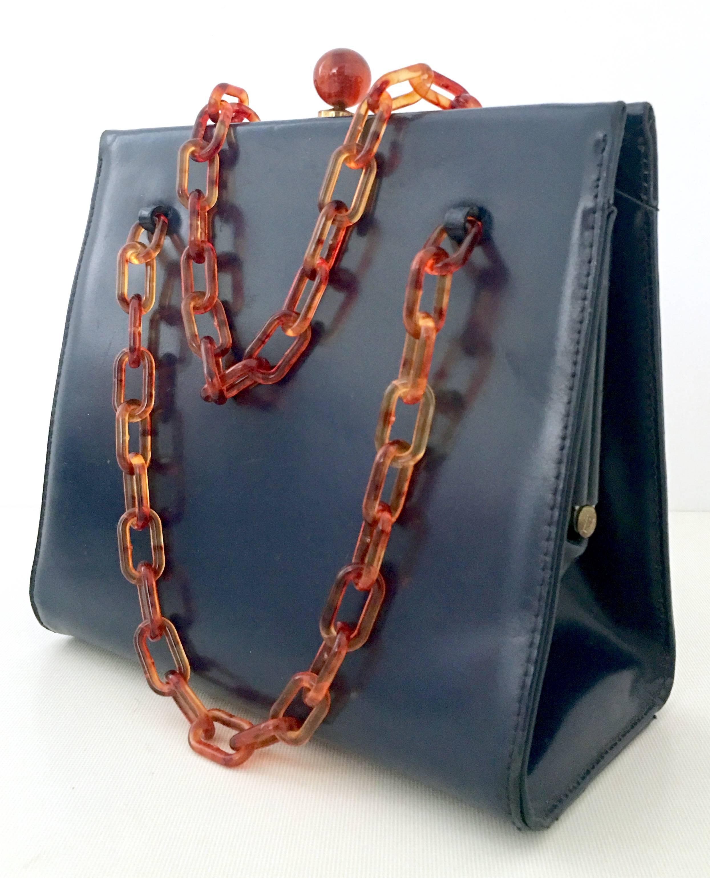 1950'S Navy Blue Leather & Faux Tortoise Bakelite Hand Bag By, Dofan France. This coveted and rare hand bag features, brass detail with a double Bakelite faux tortoise chain link shoulder strap and ball snap closure. There are four brass protective