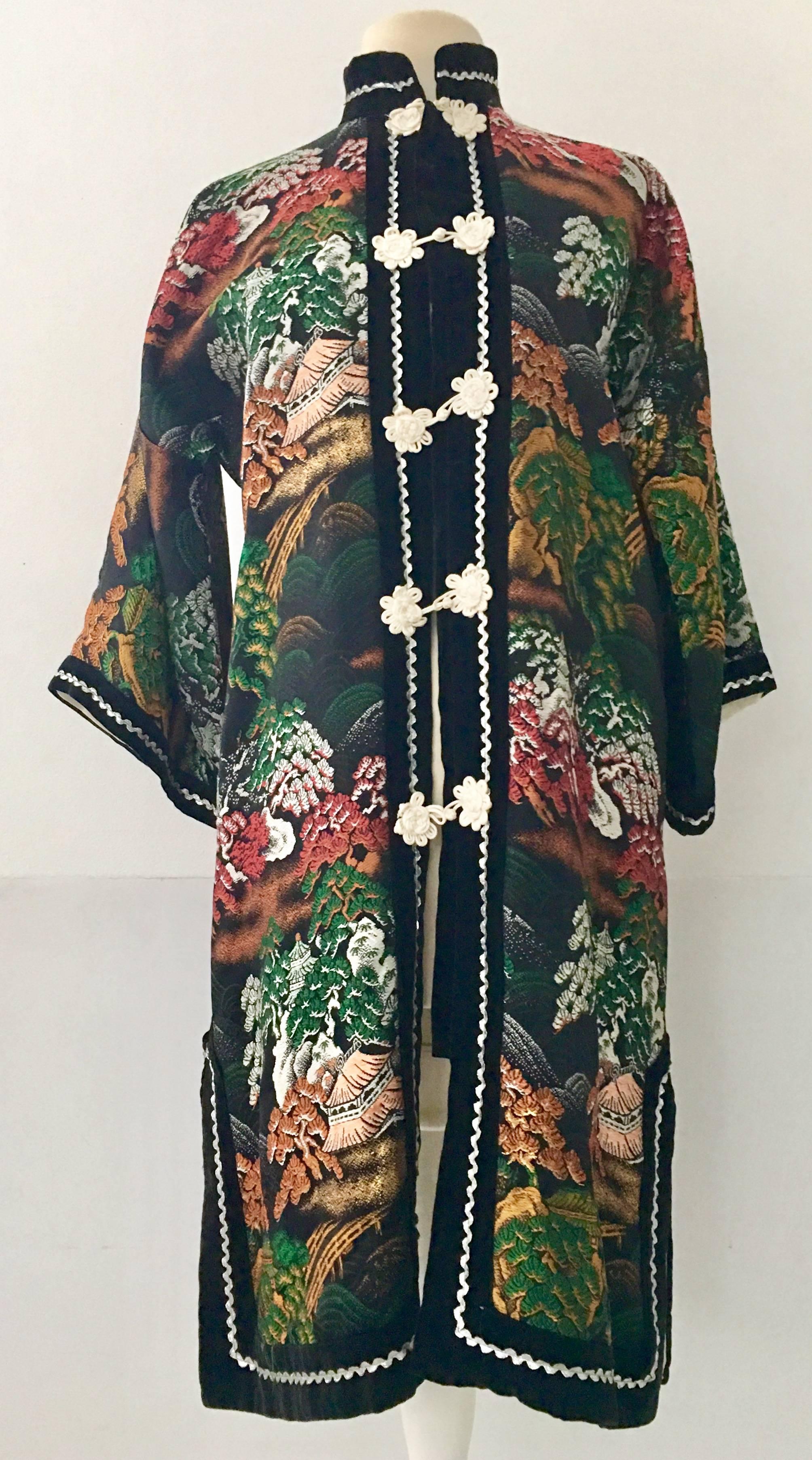 Vintage Chinoiserie Hong Embroidered Silk Jacket. Features a black ground with metallic thread embroidery in orange, emerald, peach, gold and white. Velvet trim down the front with white silk toggle style buttons and silver metallic trim finish off