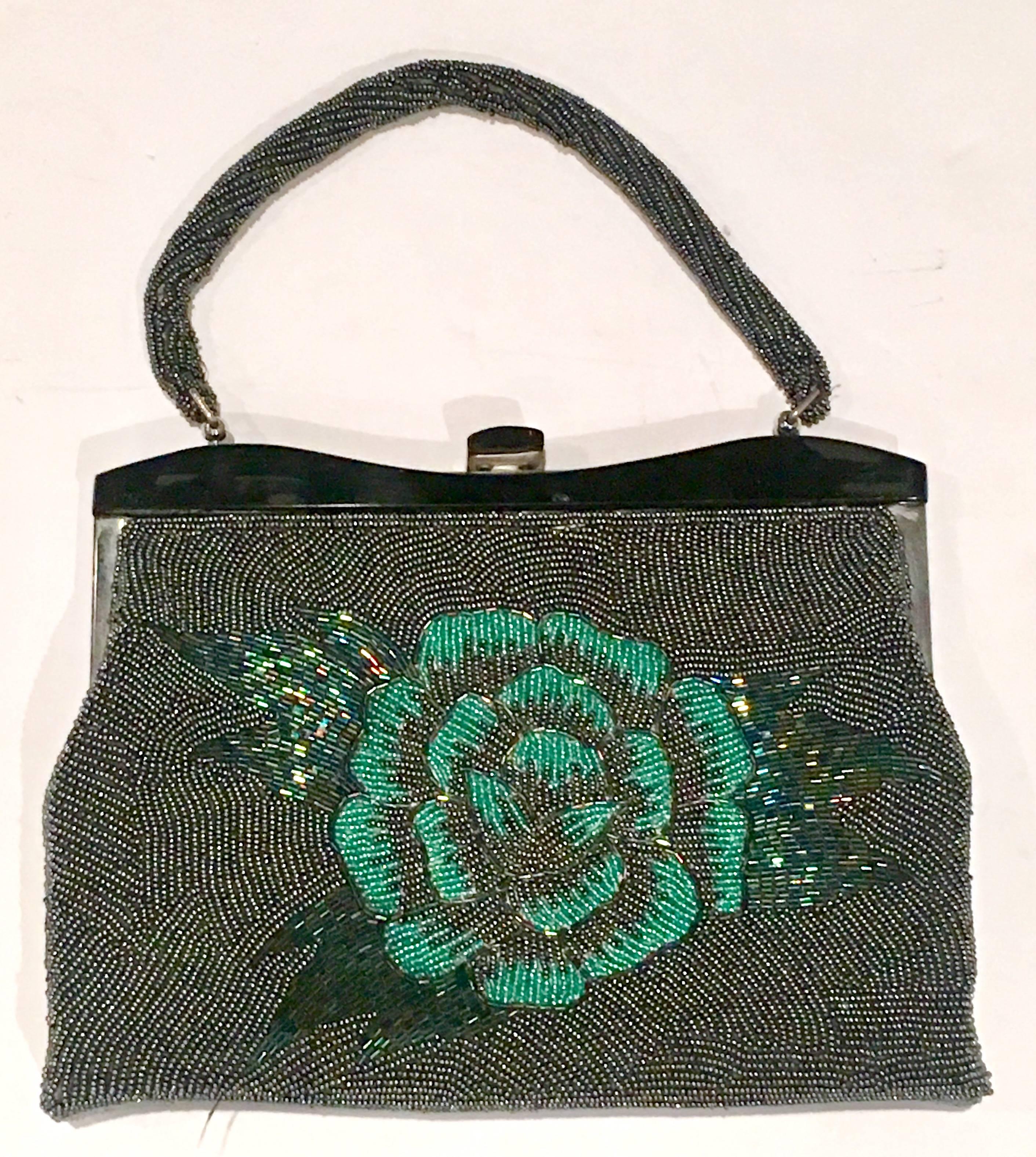 1950'S Glass Bead Handbag with chrome and black celluloid frame detail. This floral motif beaded gem features,  
a black ground with gunmetal, aqua, blue and green glass beads with a different pattern on each side. The shoulder strap is also beaded.