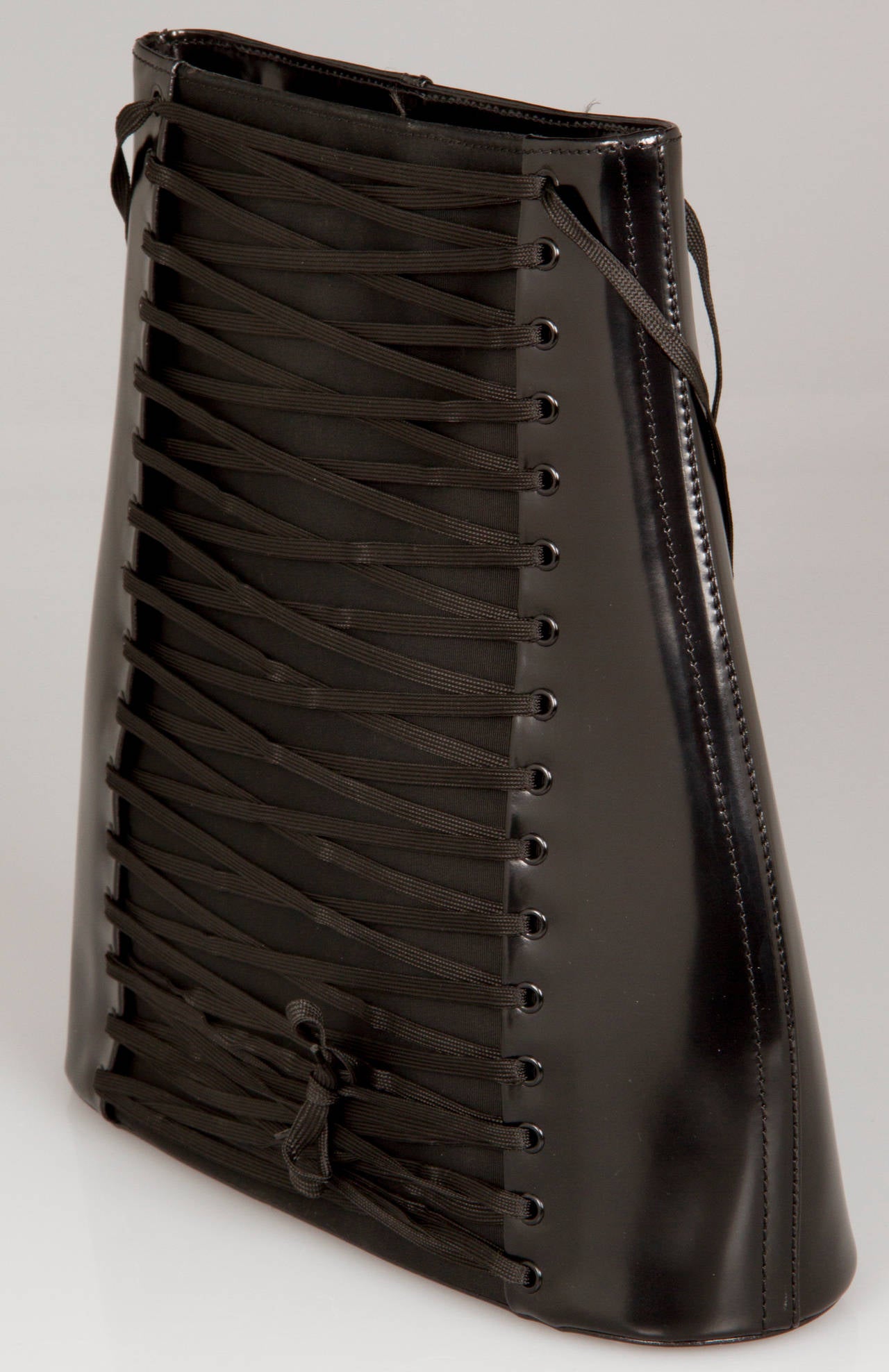 This fabulous black leather corset bag has a grosgrain panel on the front with criss-cross lacing, zippered top closure, interior zippered pocket and is  lined in black monogram fabric. It is stamped: Jean Paul Gaultier Maroquinerie.