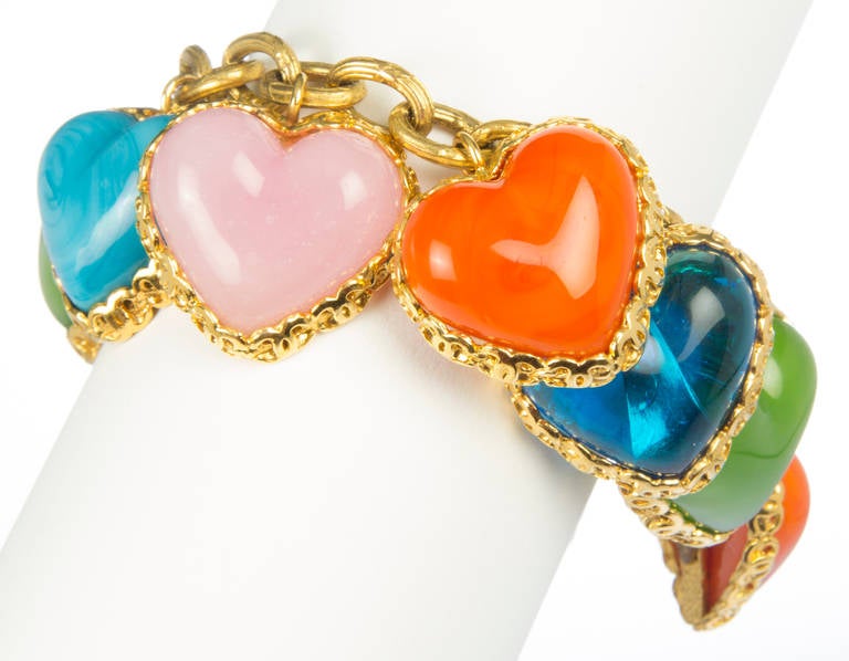 This bracelet is made of ten poured glass hearts inset in gold chain surrounds on a linked chain in a charm bracelet style.