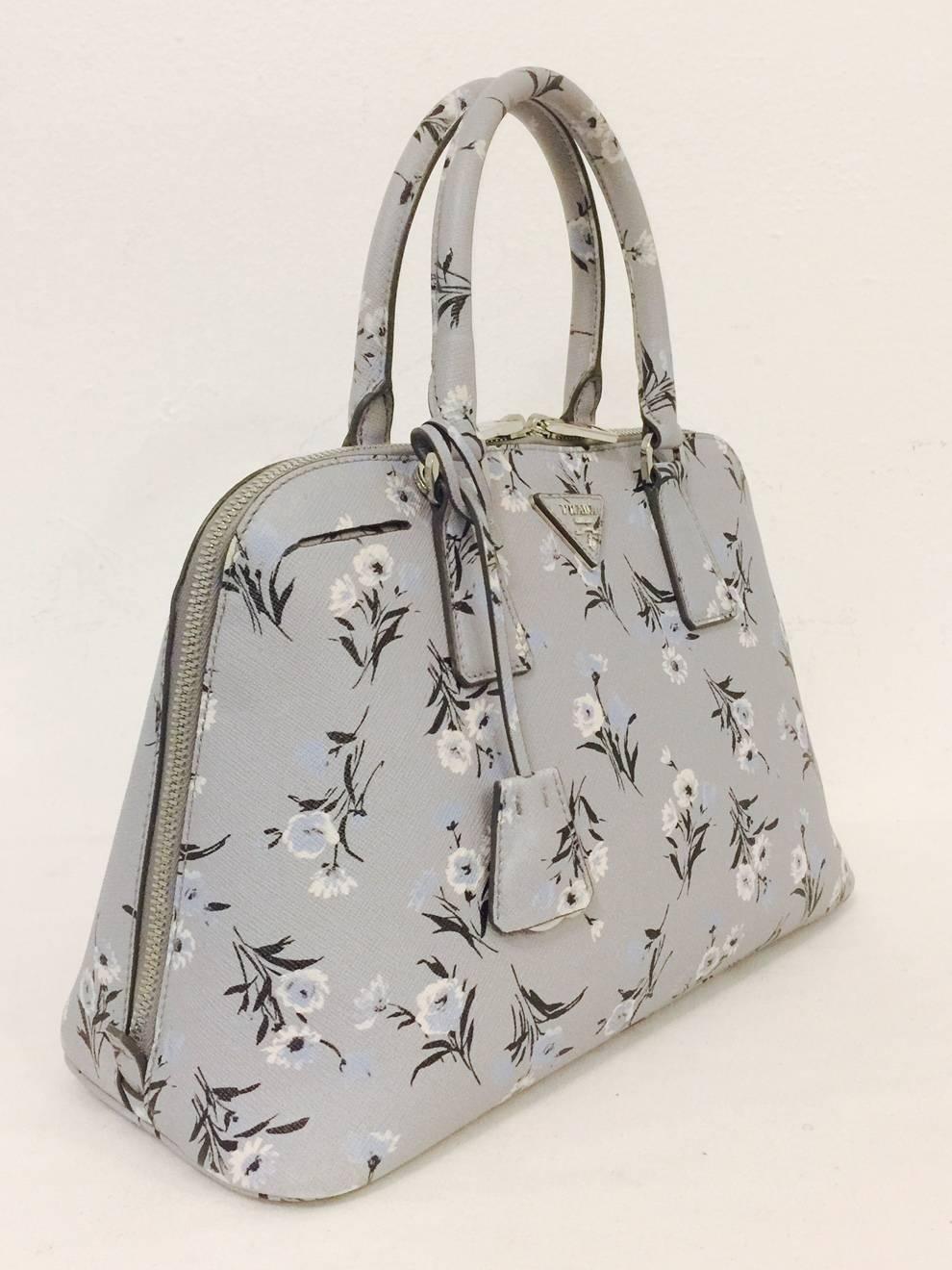 Prada Leather Satchel will quickly become a favored bag!  Features light grey floral print signature Saffiano leather, double zipper top closure, rolled handles, and, and detachable crossbody shoulder strap.  Logo jacquard lining.  Interior houses