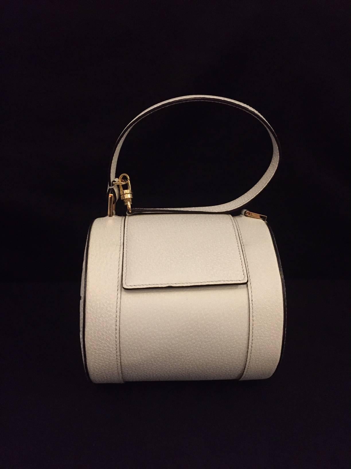 Bvlgari crafts much more than some of the world's most highly desired fine jewelry!  Ivory textured leather cylindrical bag features geometric shape, Gold tone hardware and flap.  Boasts iconic "BVLGARI" logo on both sides.  Magnetic Snap