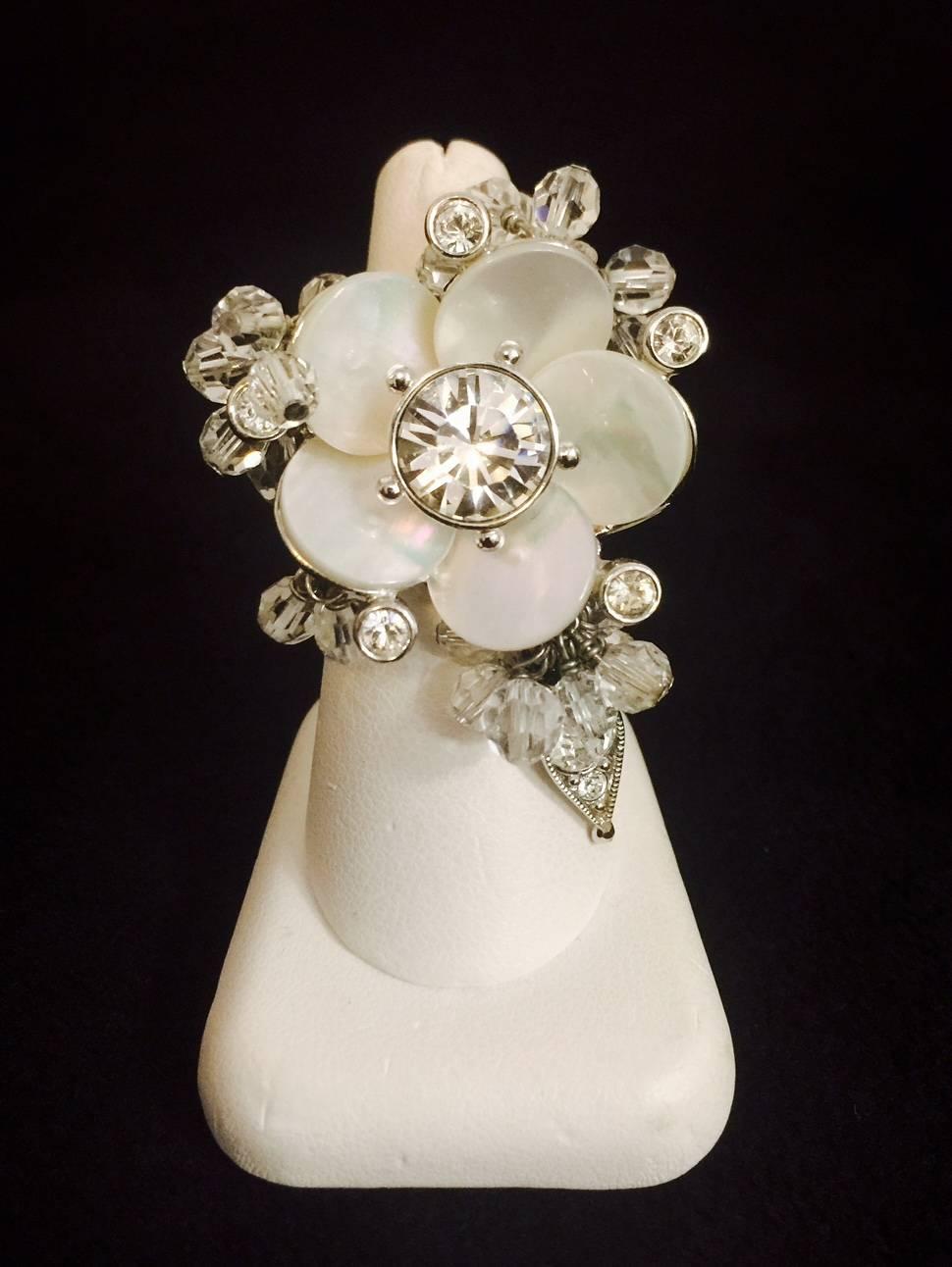 From the world renowned Dior comes this delightful ring in silver tone featuring a centered flower crafted in shell mother of pearl. Wide, thick, substantial tapered shank. Three dangling sections are fabricated with Swarovski crystals and faceted
