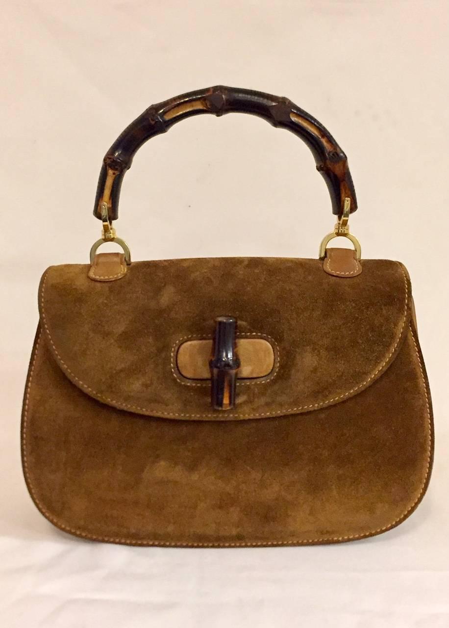 Gucci Carob suede medium handbag with single top bamboo handle features gold tone hardware on handle and bamboo accented turn lock closure on front flap.  Tonal stitching throughout, tan leather lining, one pocket at interior wall and snap closure