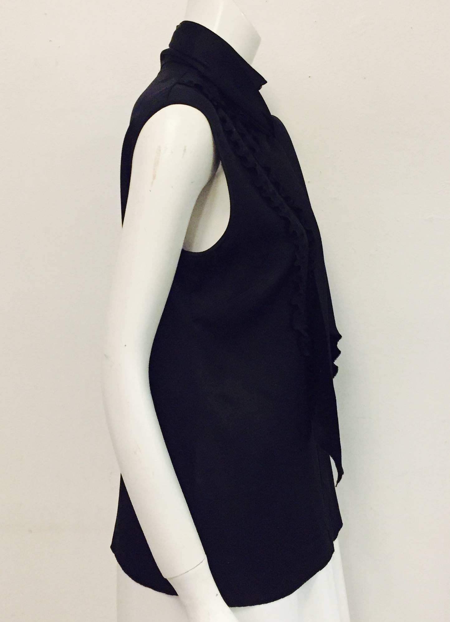 This charming Chanel black silk sleeveless tuxedo style top takes the top hat, pun intended!   Three ruffles on each side of the blouse meeting at the center of blouse with hidden closure and 9 Chanel logo buttons.  Possesses an up collar with 3