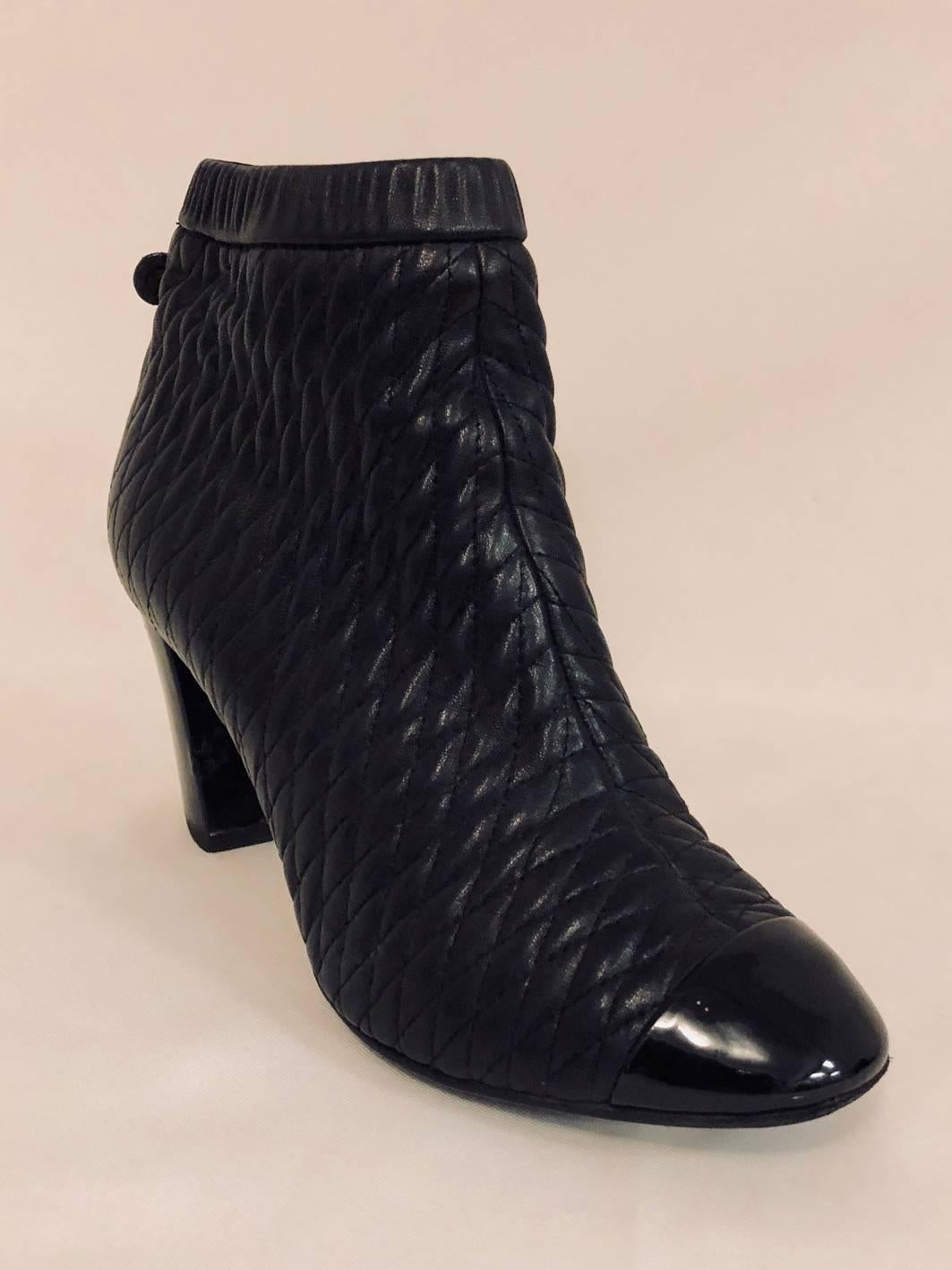 Chanel black quilted leather ankle booties with round patent leather cap toe and heels featuring white interlocking CC logo at top of heel.  For easy access these booties possess a side zipper closure.   In good condition showing some wear on the